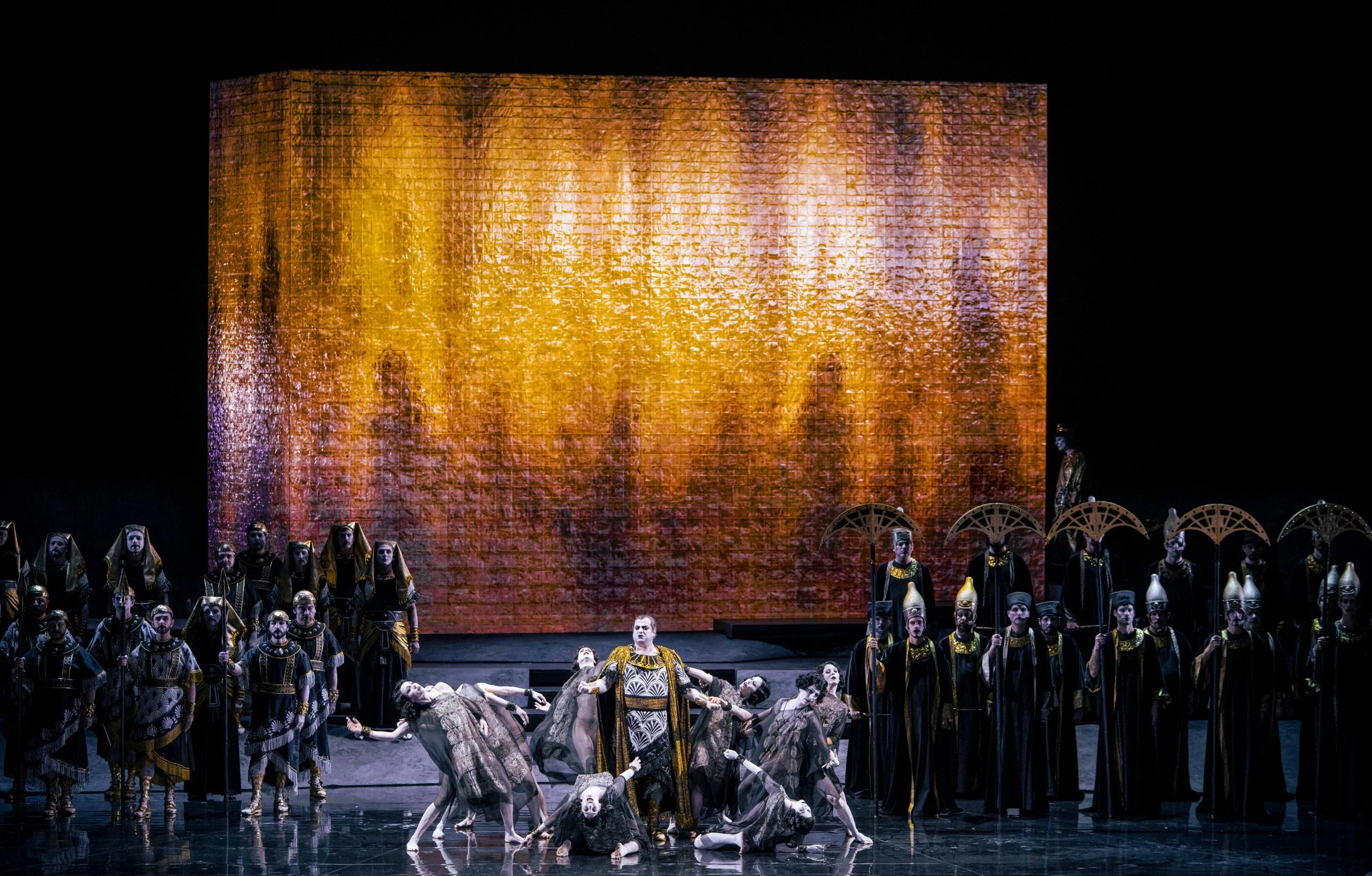 Dancers around a soloist at the front of the stage, chorus at the sides and a glowing amber block behind – Aida at Opéra de Monte-Carlo, Monte Carlo, Monaco, 2025 – set design
