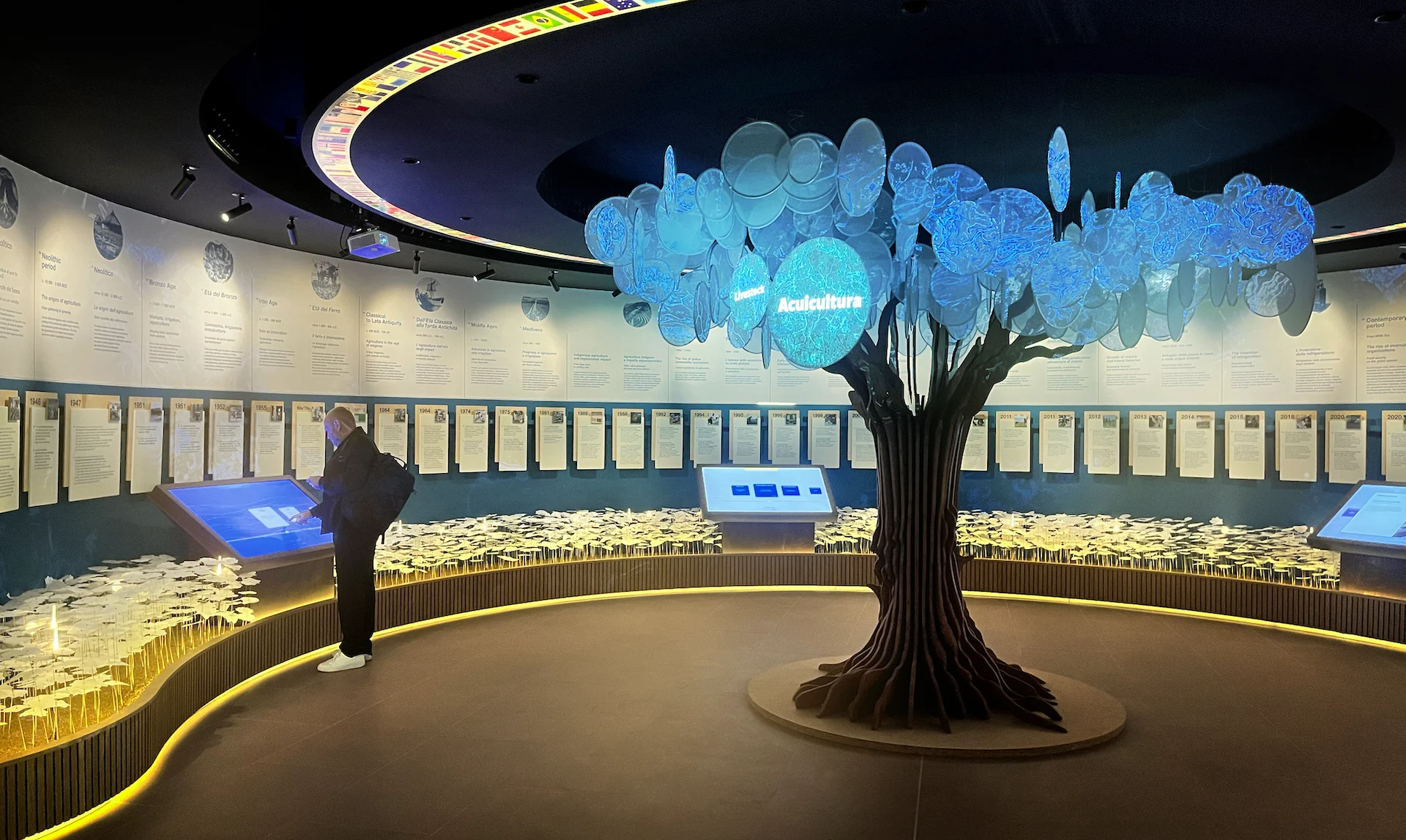 Circular museum room with a glowing tree of illuminated discs, touch screens and wall panels around it – FAO MuNe Food and Agriculture Museum, Rome, Italy, 2025 – exhibition design