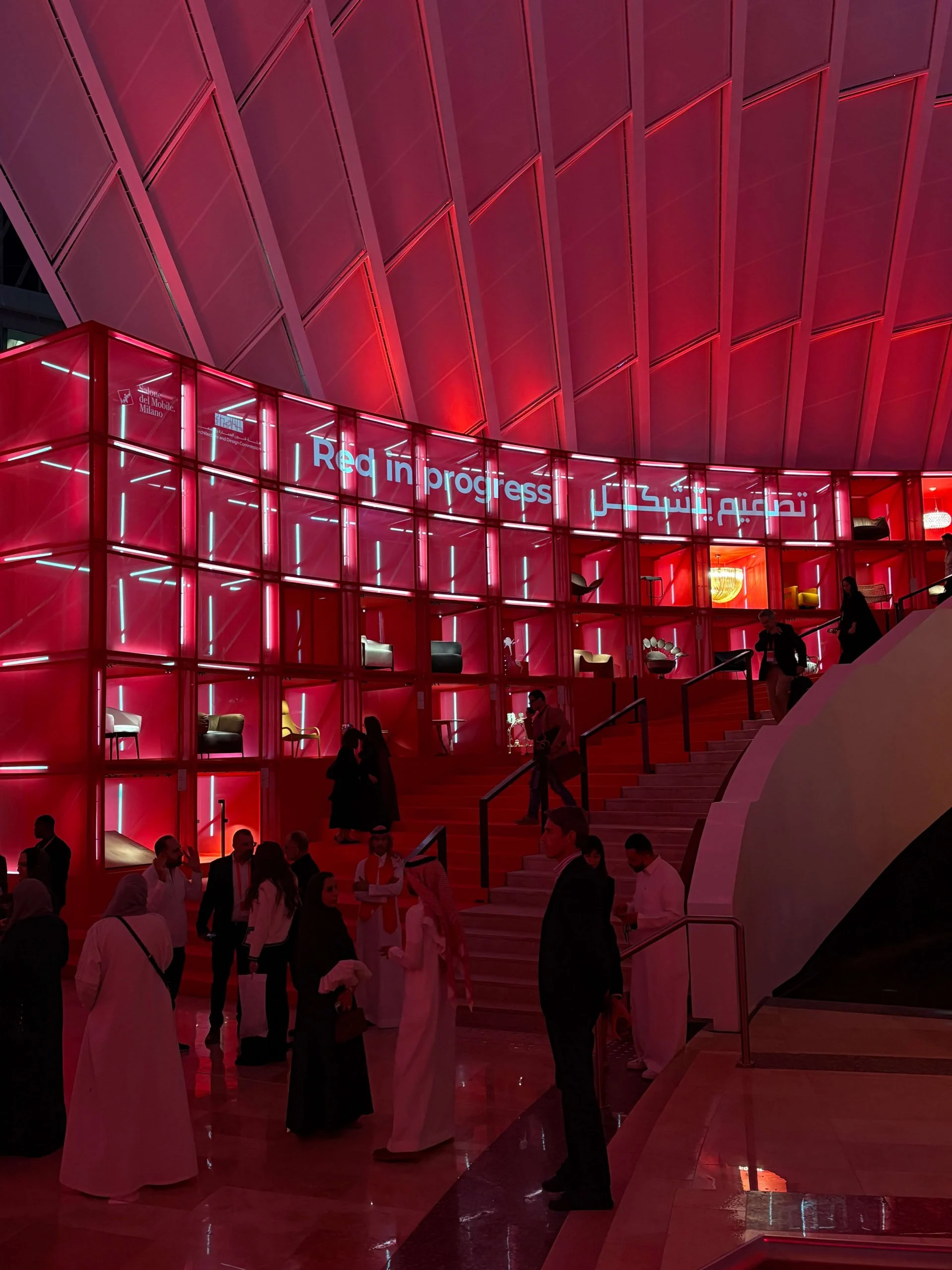 Evening crowd at the foot of the illuminated red display wall and staircase – Red in Progress: Salone del Mobile Meets Riyadh, Saudi Arabia, 2025 – exhibition design