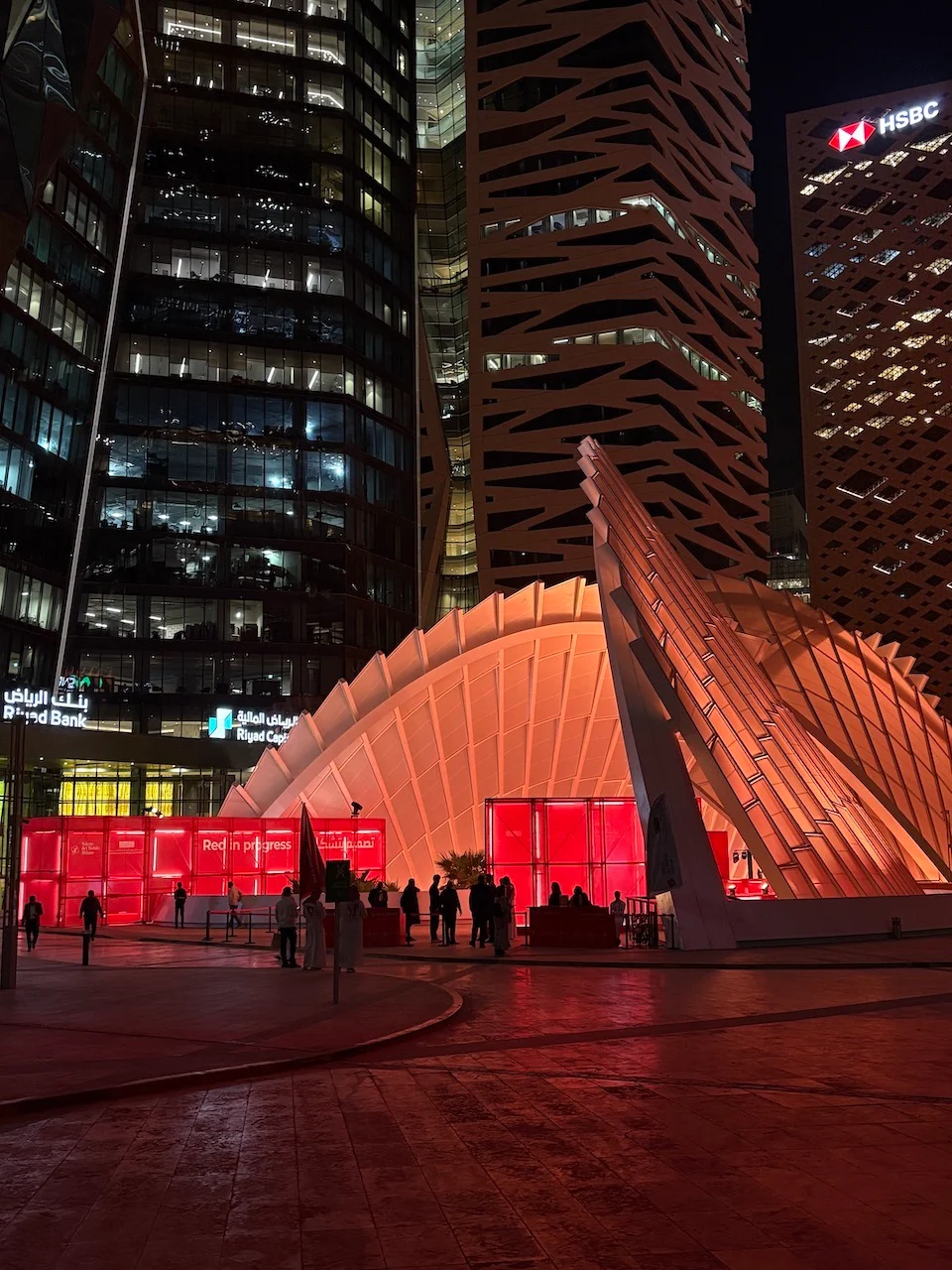 Night view of the installation glowing red beneath a lit canopy among the KAFD towers in Riyadh – Red in Progress: Salone del Mobile Meets Riyadh, Saudi Arabia, 2025 – exhibition design