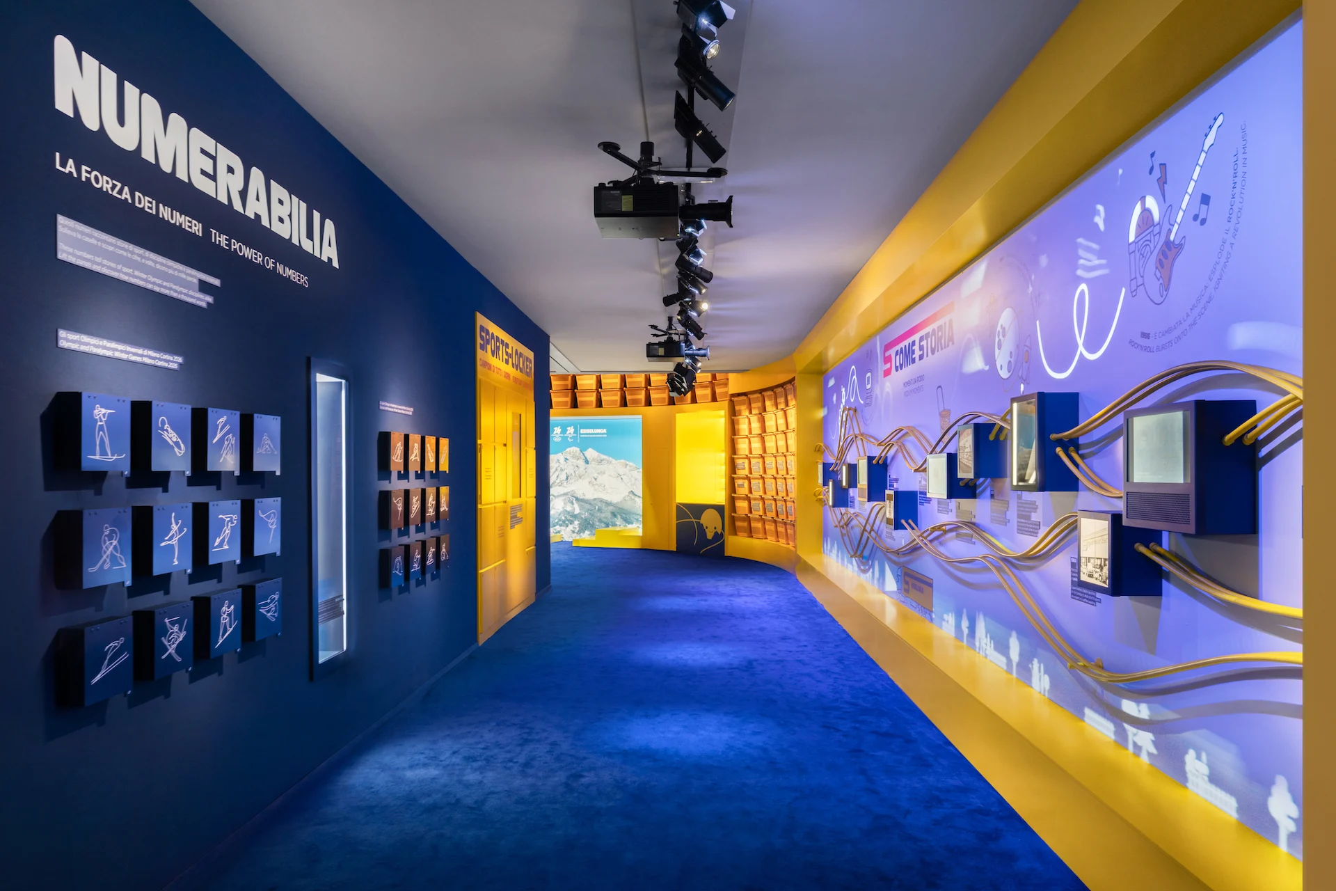 Blue-carpeted corridor with the Numerabilia wall of sport pictograms on the left and an illustrated timeline on the right – Casa Esselunga at Milano Cortina 2026, Italy – exhibition design