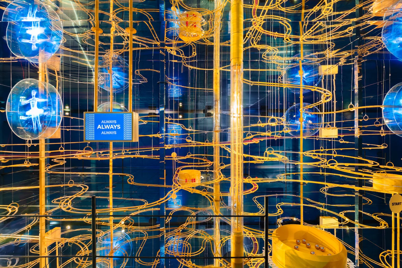 Wide view of the marble-run installation: golden tracks, glowing athlete holograms and a screen reading ALWAYS – Casa Esselunga at Milano Cortina 2026, Italy – exhibition design