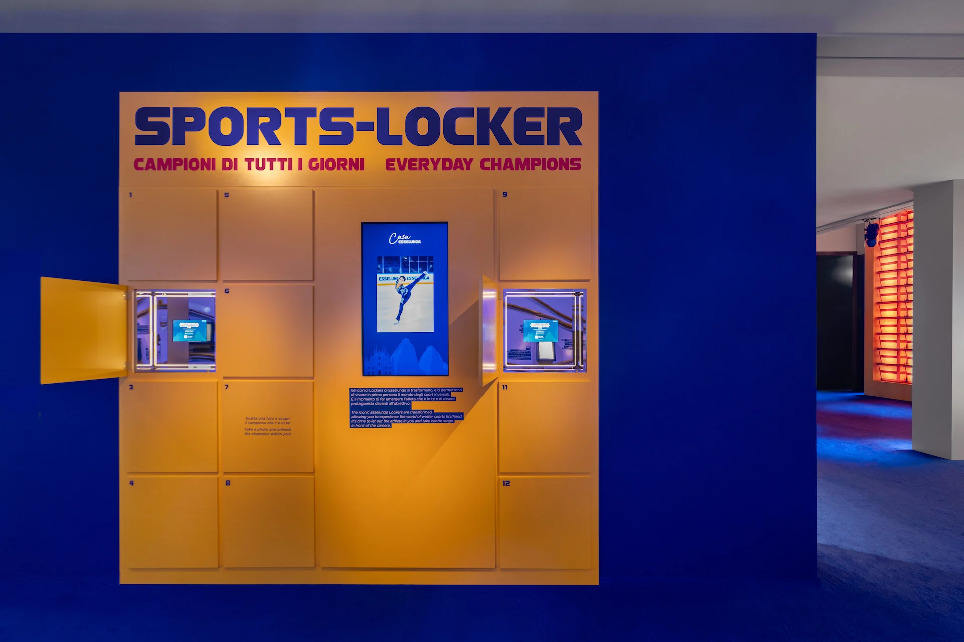 Yellow Sports-Locker wall with open doors revealing small screens, set in a deep blue room – Casa Esselunga at Milano Cortina 2026, Italy – exhibition design