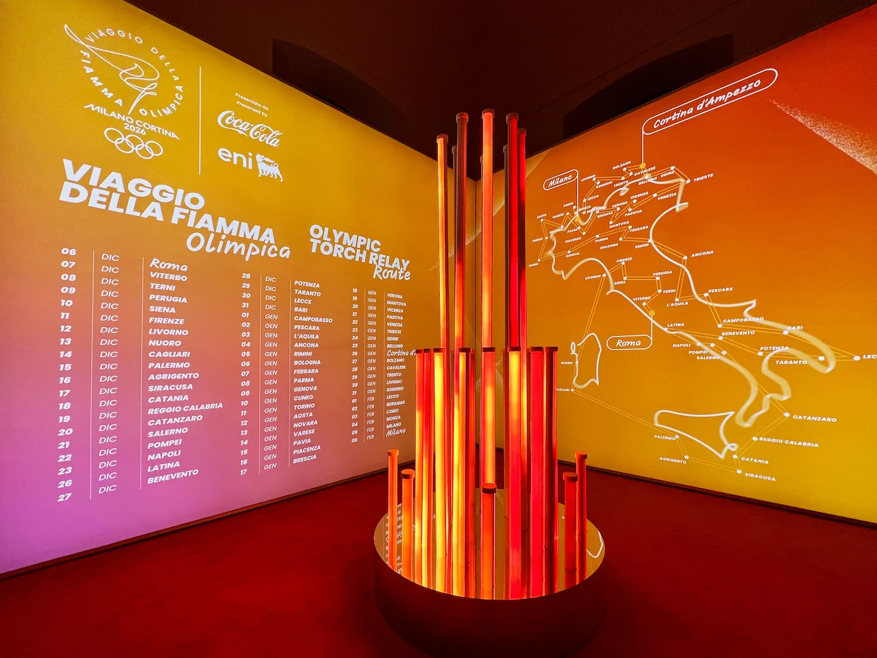Torch relay room: glowing red and orange tube sculpture before walls with the route map of Italy – Clubhouse 26 Milano, Italy, 2026 – hospitality design