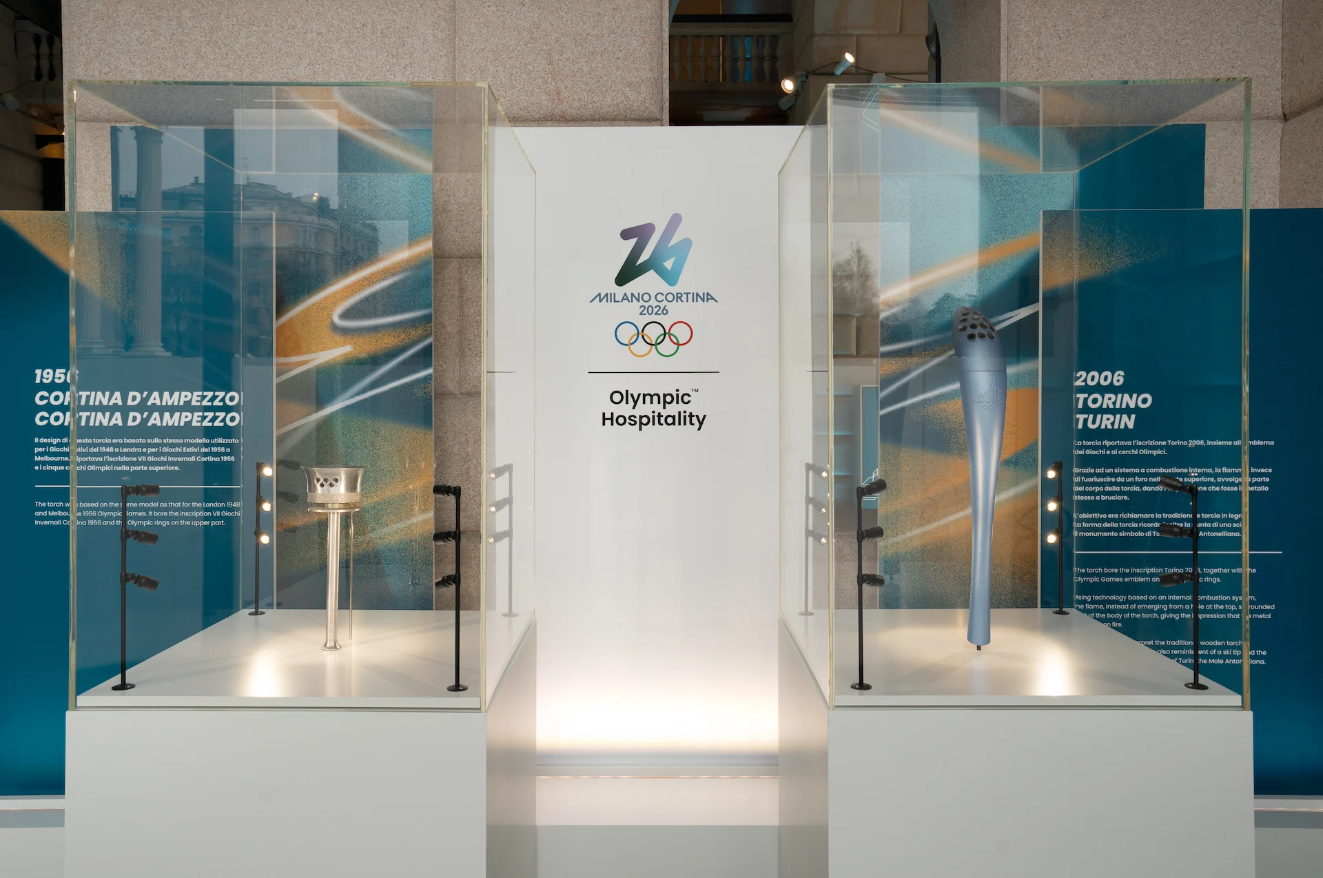 Glass cases with the 1956 Cortina and 2006 Turin Olympic torches, flanking a Milano Cortina 2026 panel – Clubhouse 26 Milano, Italy, 2026 – hospitality design