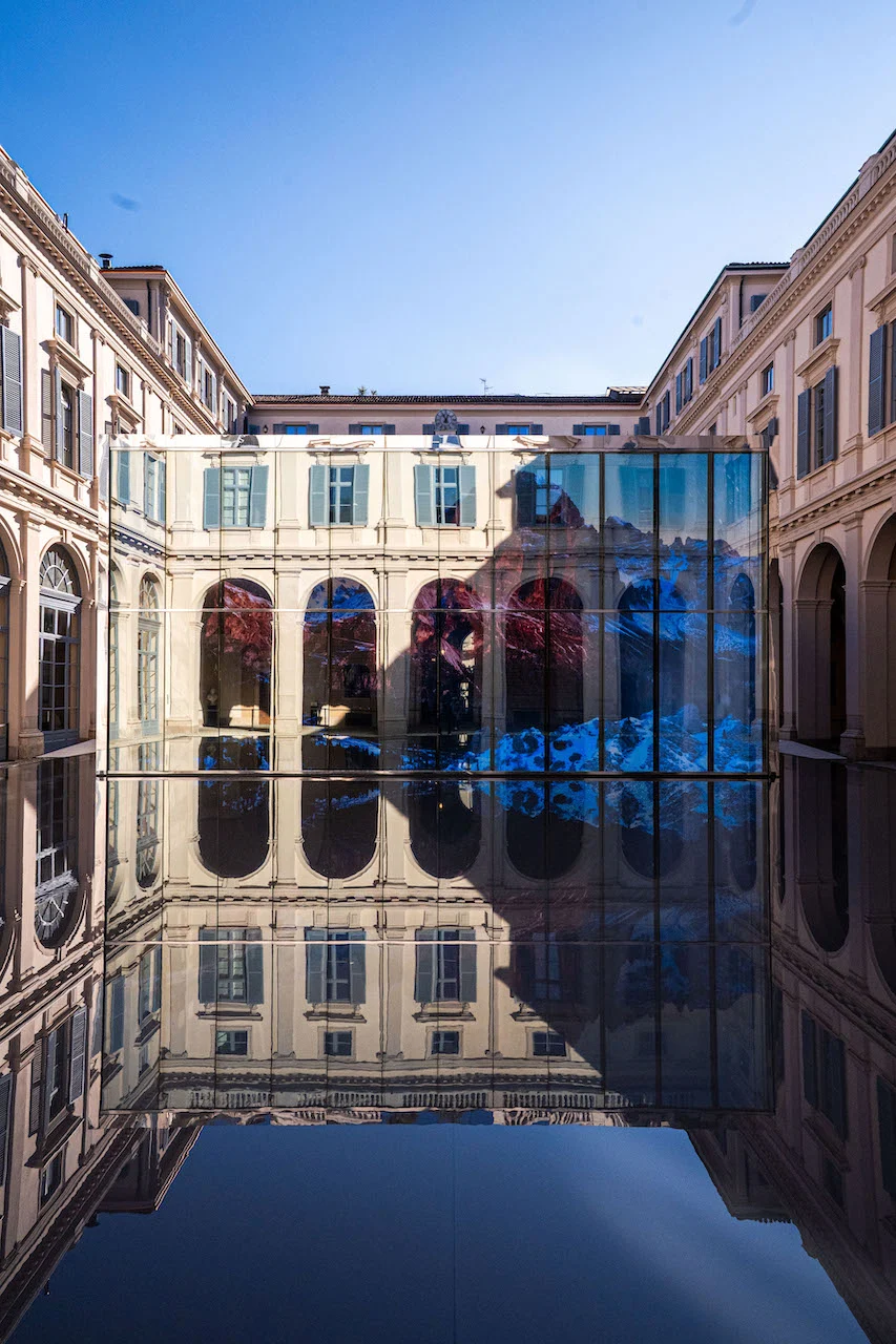 Glass pavilion showing a snowy mountain image, reflected with the courtyard arcades in the dark pool – Samsung House at Palazzo Serbelloni, Milan, Italy, 2026 – interior design