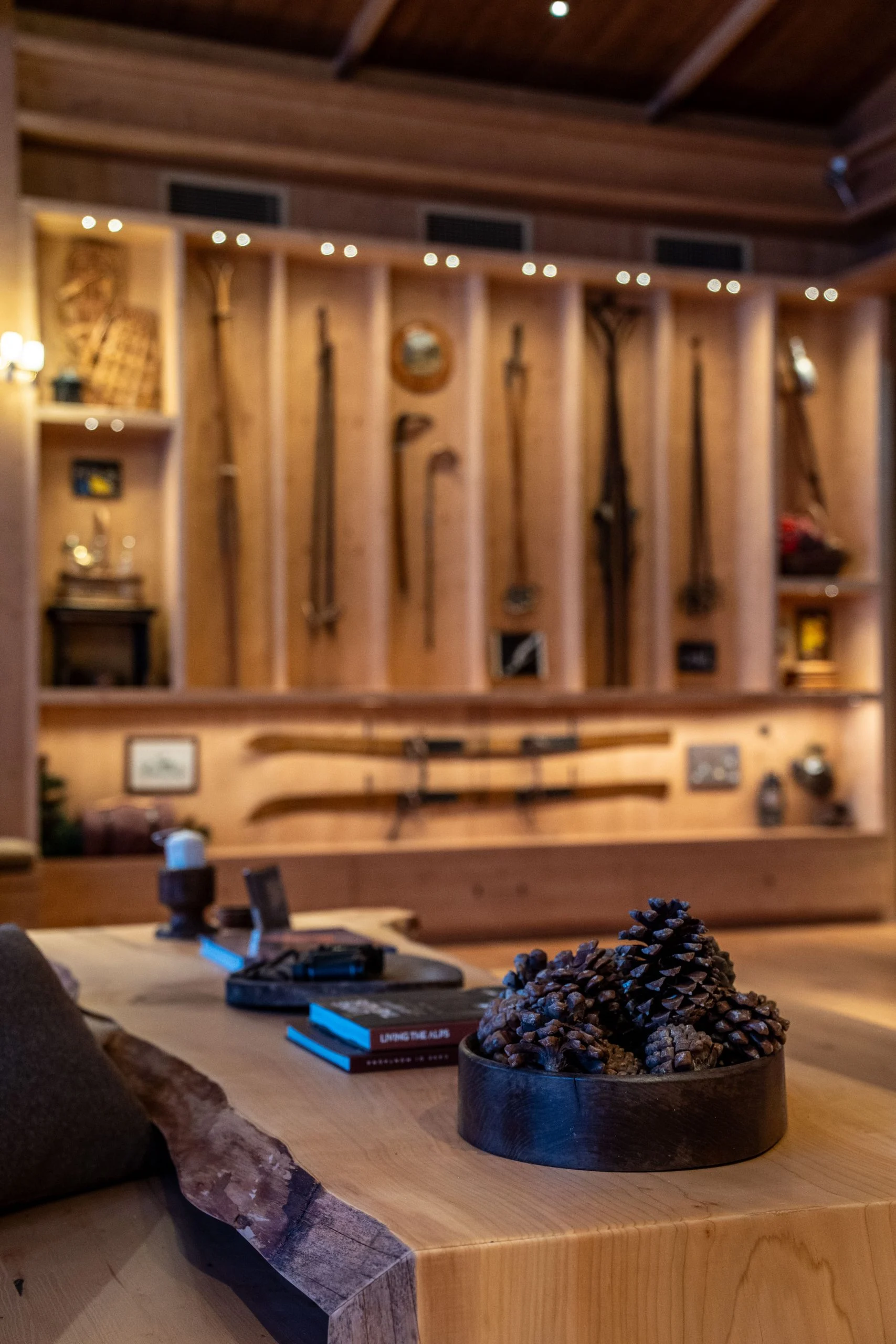 Live-edge wooden table with pine cones before a lit display of vintage skis and alpine equipment – Samsung House at Palazzo Serbelloni, Milan, Italy, 2026 – interior design