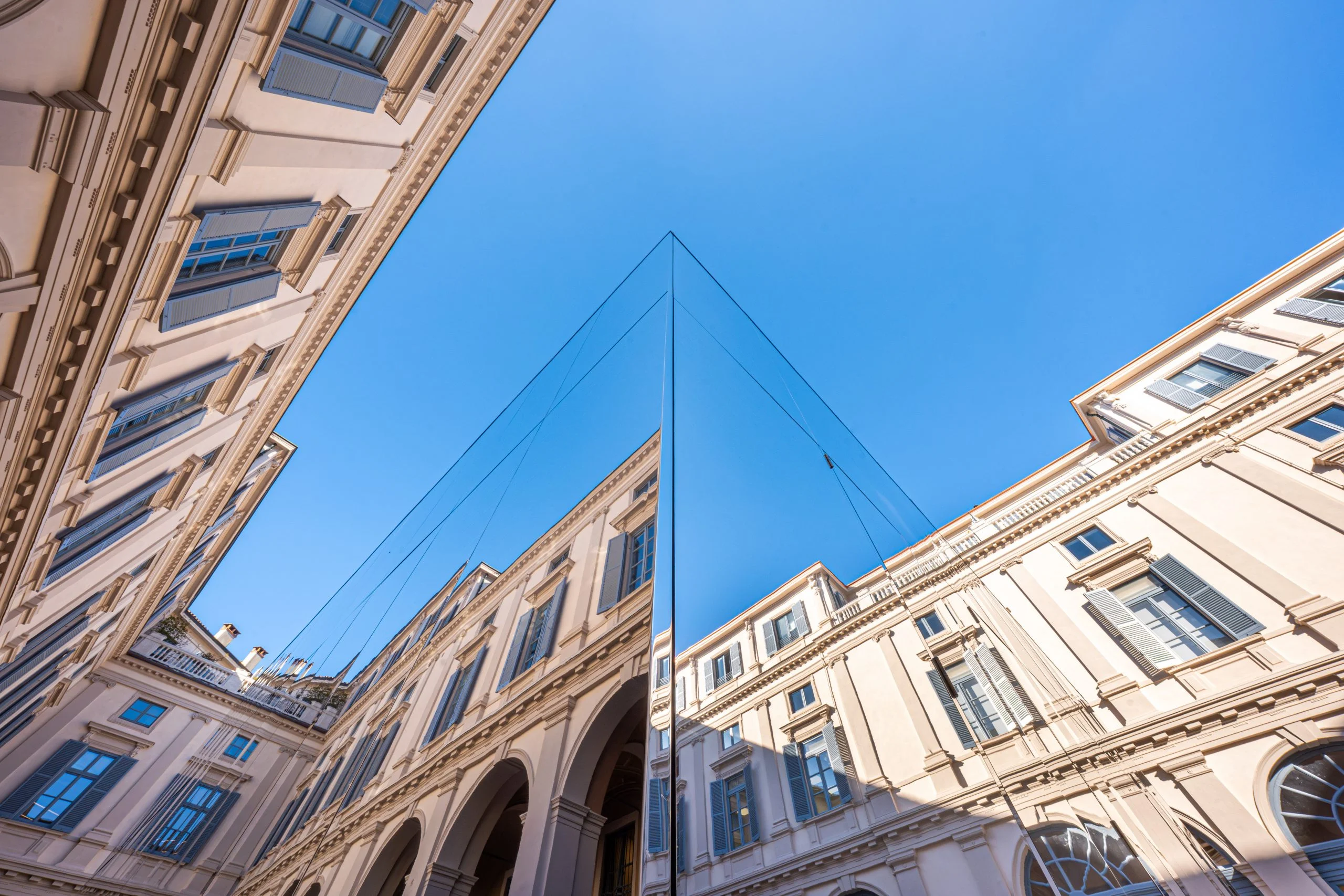 Upward view of the mirrored pavilion corner reflecting the palazzo façades against a clear blue sky – Samsung House at Palazzo Serbelloni, Milan, Italy, 2026 – interior design