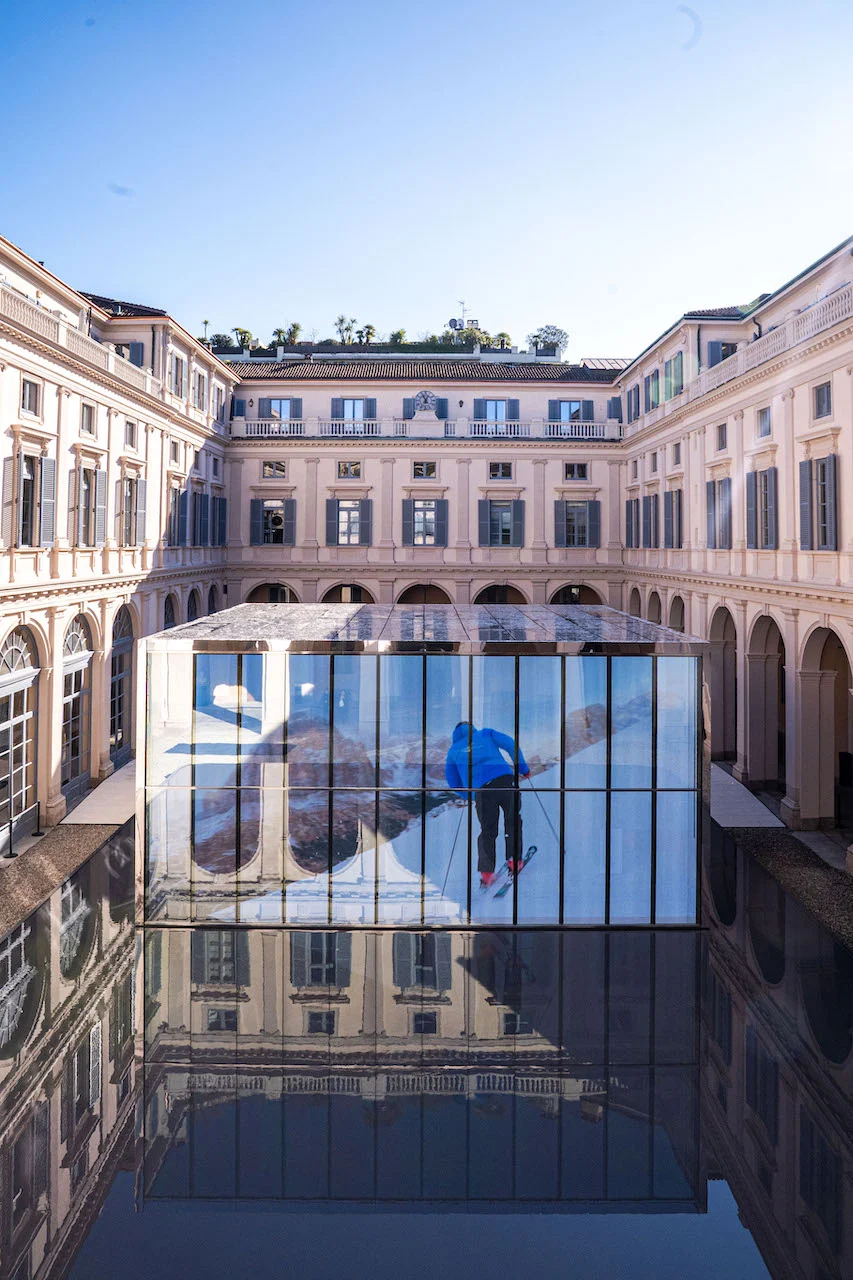 Glass pavilion in the courtyard showing a skier on a giant screen, mirrored in the black pool – Samsung House at Palazzo Serbelloni, Milan, Italy, 2026 – interior design