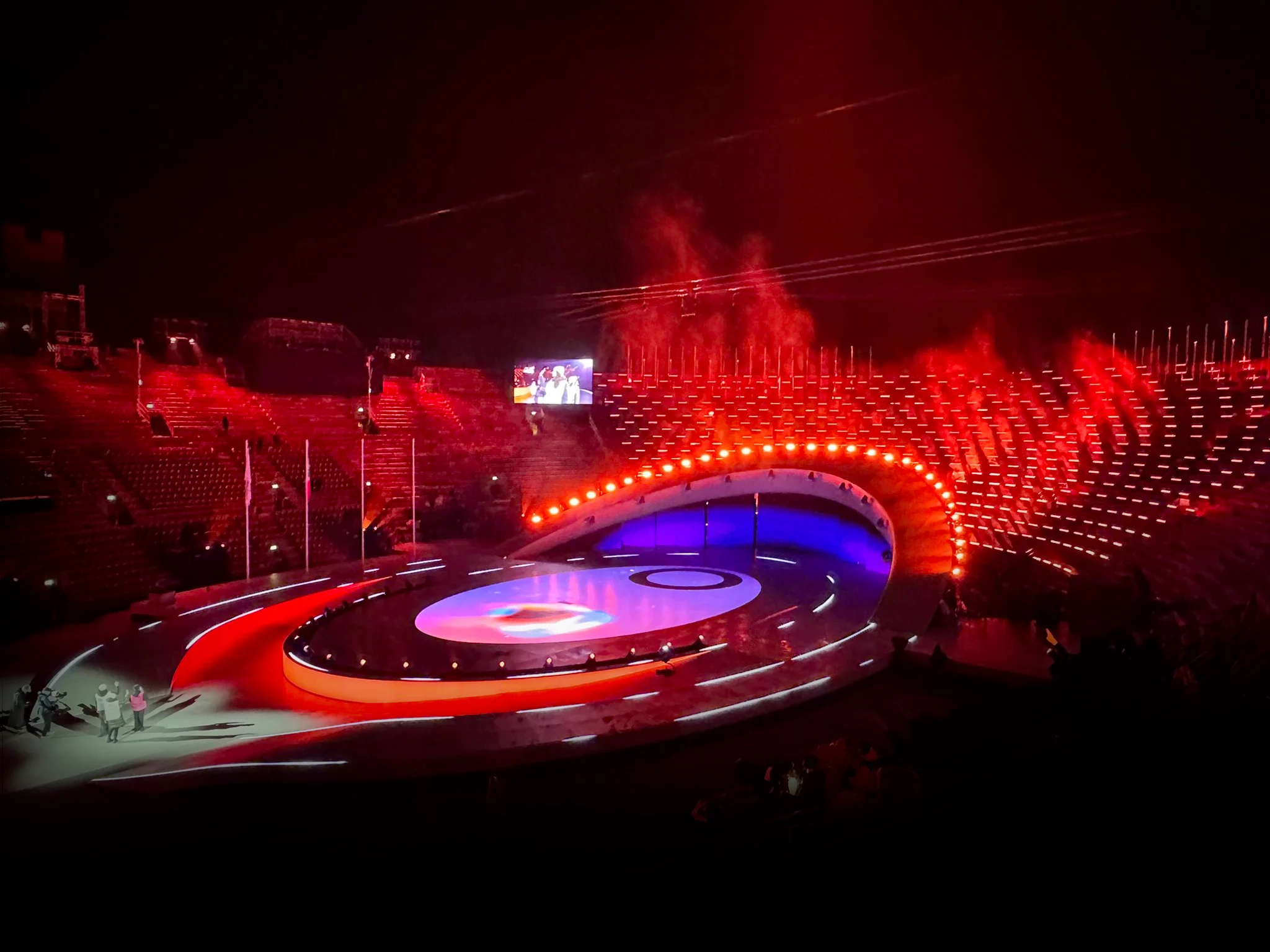 Stage and arena steps bathed in red light, with a row of lights along the curved arch – Milano Cortina 2026 Olympic Closing Ceremony, Verona, Italy – stage design