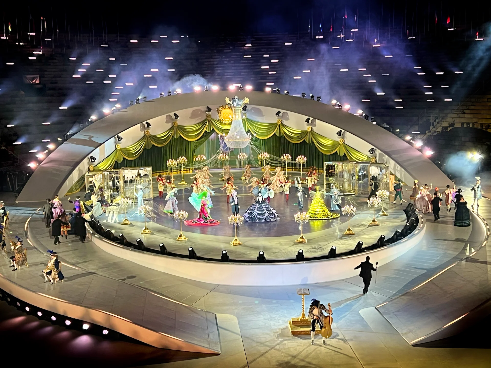 Performers in Baroque-style costumes and gowns on the central stage, framed by green and gold drapes – Milano Cortina 2026 Olympic Closing Ceremony, Verona, Italy – stage design