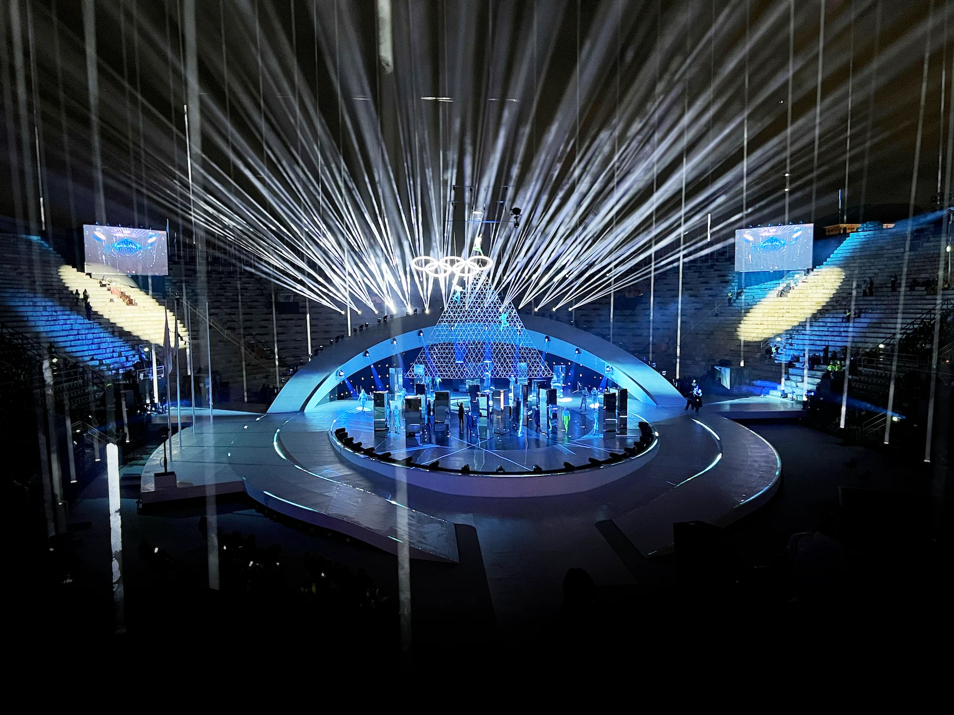 Wide view of the closing ceremony stage in the Arena di Verona: oval platform under a curved arch and white light beams – Milano Cortina 2026 Olympic Closing Ceremony, Verona, Italy – stage design