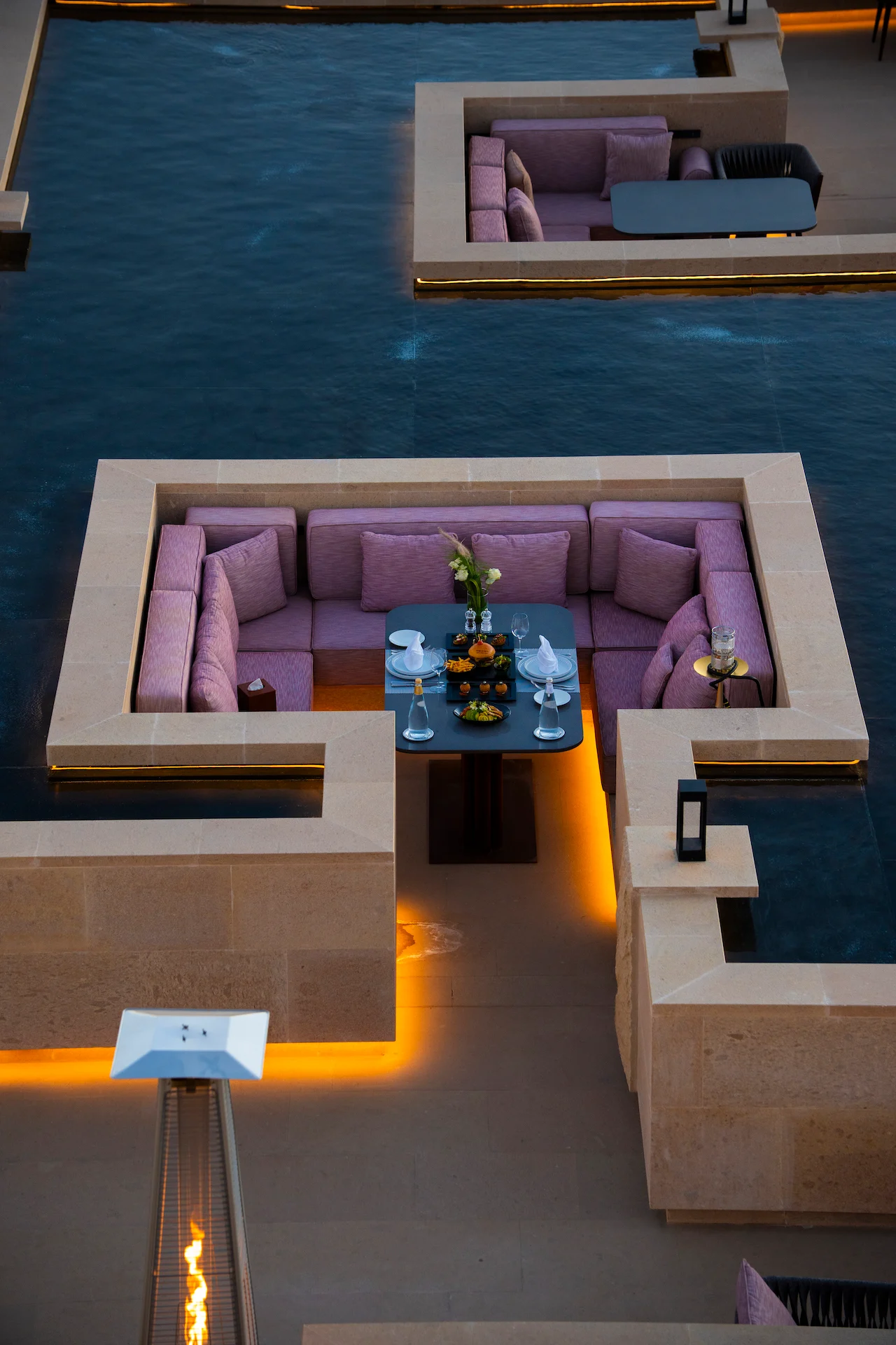 Sunken booth with pink cushions and a laid table, surrounded by water in the stone basin – Sky View Restaurant at The Chedi Hegra, AlUla, Saudi Arabia, 2026 – architecture