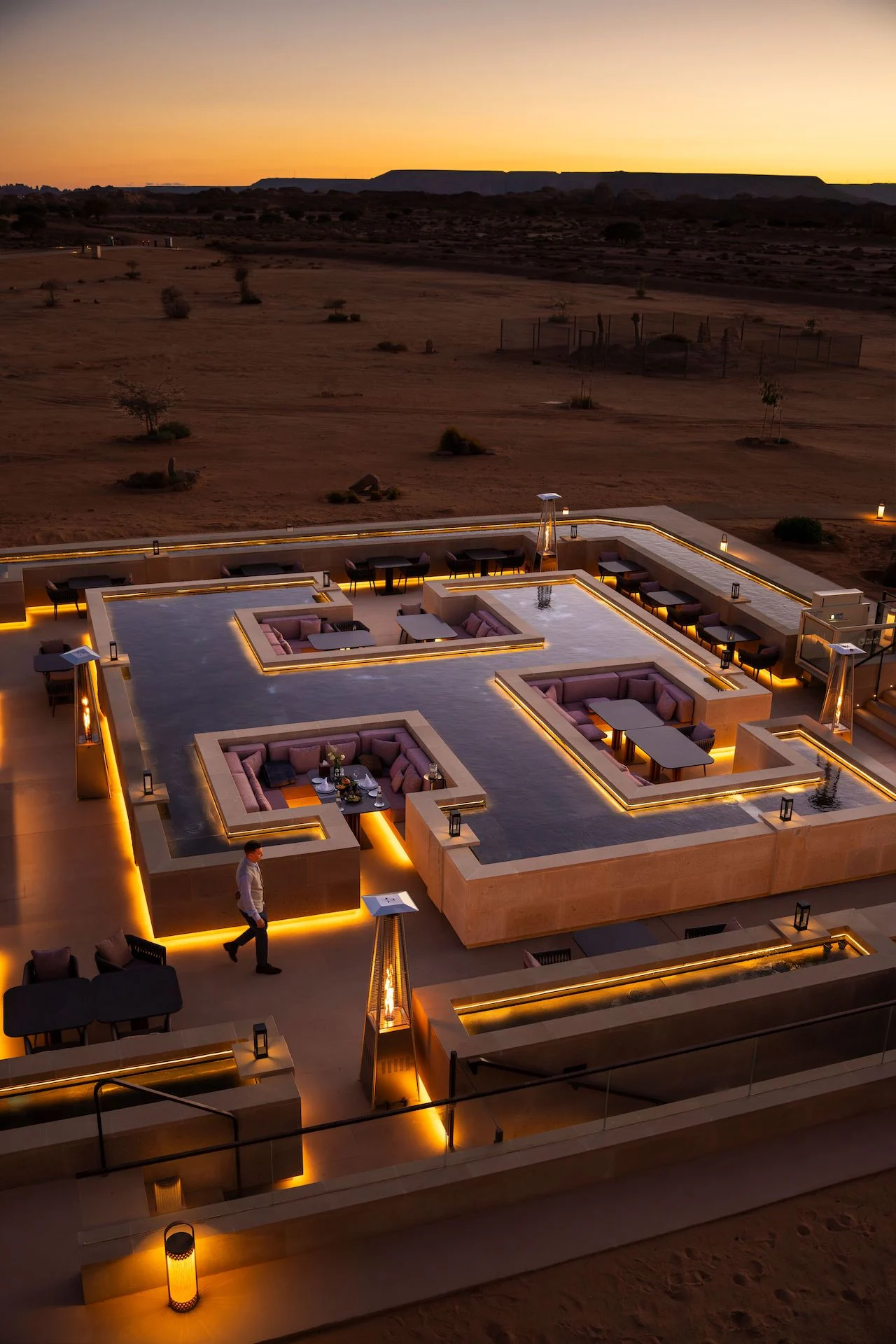 Sky View Restaurant at dusk from above: sunken lounges set in a dark reflecting basin, desert beyond – Sky View Restaurant at The Chedi Hegra, AlUla, Saudi Arabia, 2026 – architecture