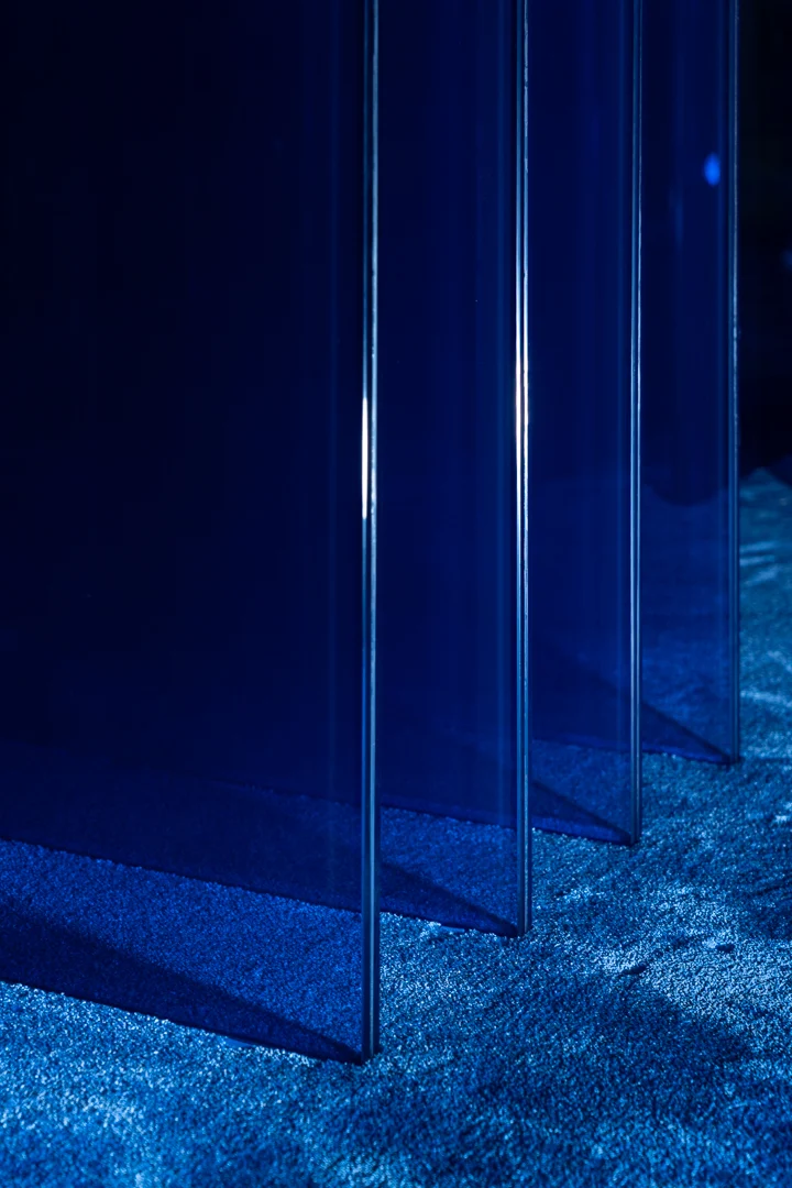 Detail of the blue glass panels of the base casting shadows on the blue carpet – STRACTA Table for Driade, Milan, Italy, 2026 – product design