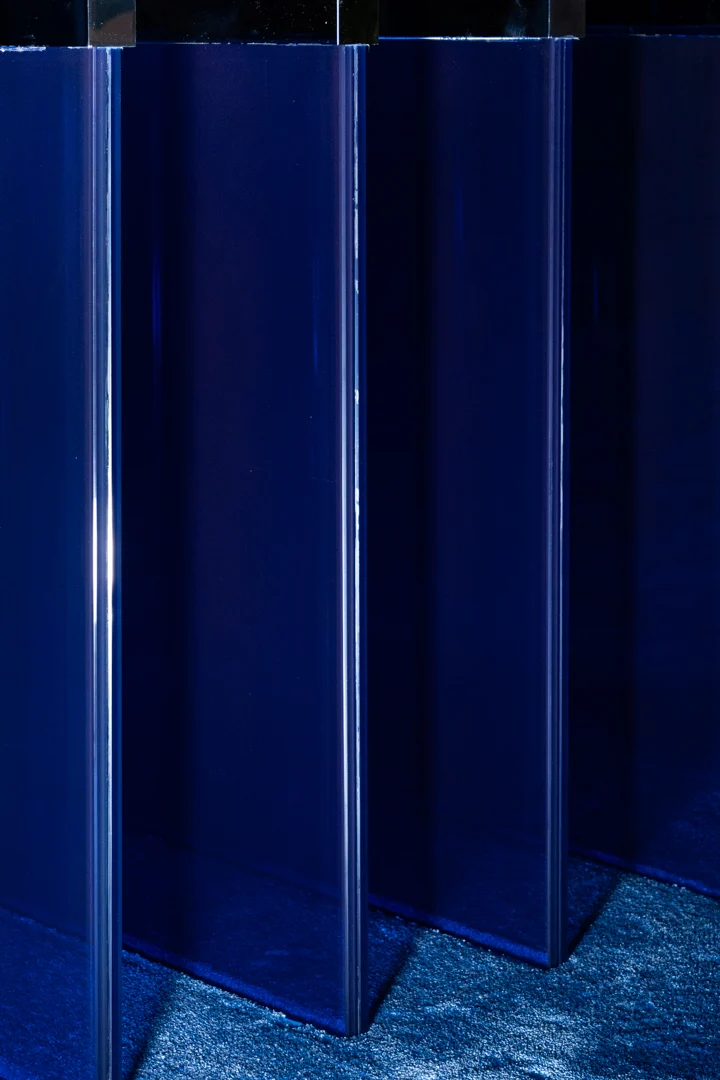Close-up of overlapping deep blue glass panels of the table base, seen from a low angle – STRACTA Table for Driade, Milan, Italy, 2026 – product design