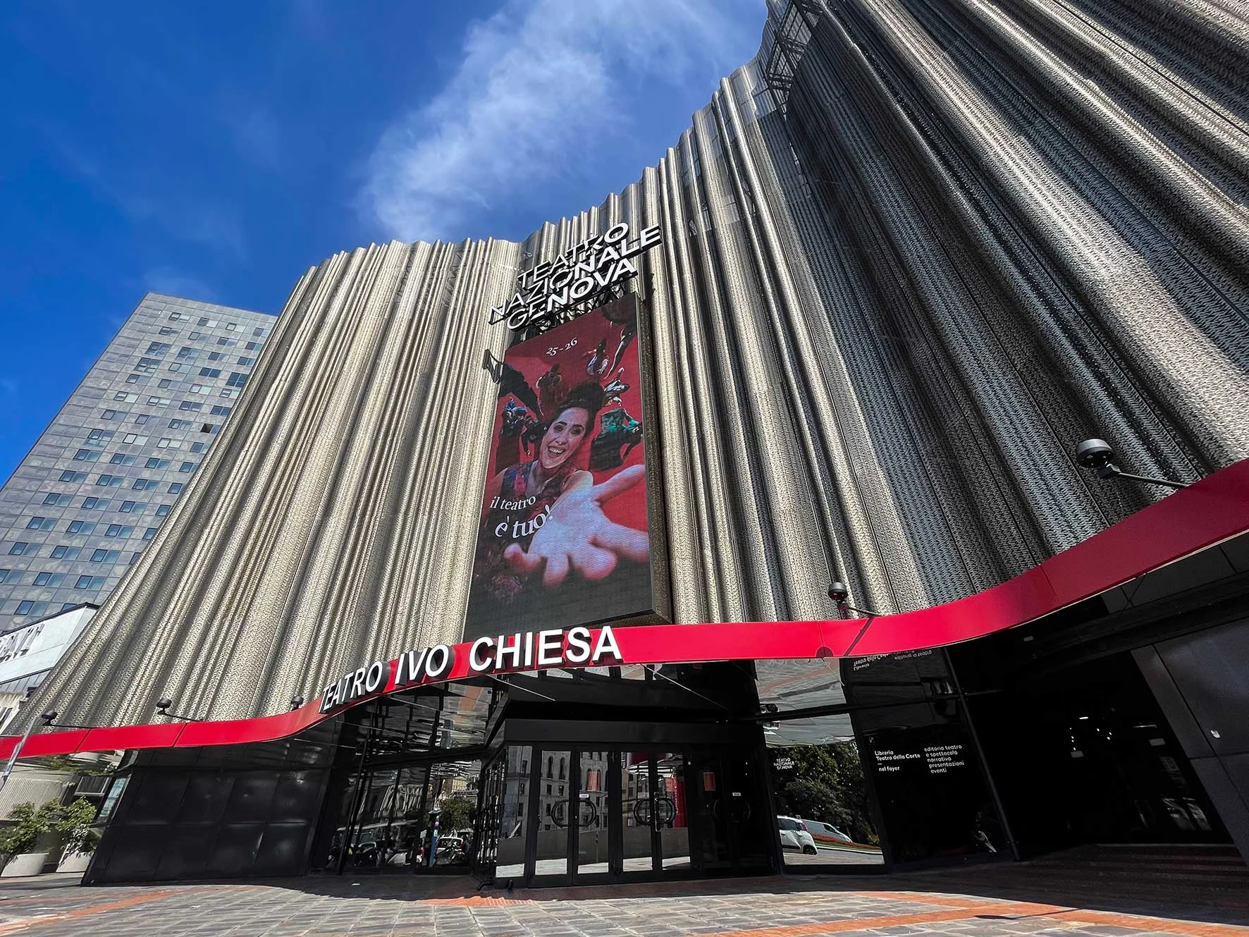 Low-angle view of the Teatro Nazionale Ivo Chiesa façade: a pleated metal curtain over a red entrance canopy – Teatro Nazionale Ivo Chiesa Façade, Genoa, Italy, 2025 – architectural refurbishment