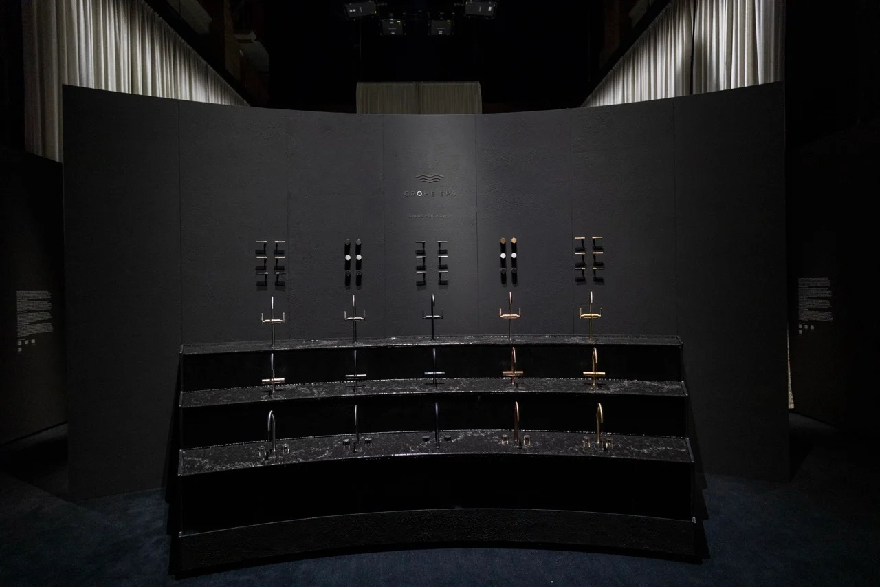 Curved dark display wall with rows of taps in different finishes on stepped black stone counters – GROHE SPA Aqua Sanctuary at Fuorisalone, Milan, Italy, 2026 – installation design