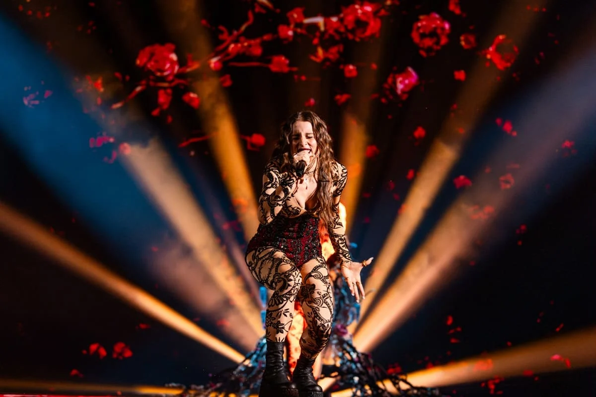 Singer crouching mid-performance under red rose projections and fanned orange light beams – Angelina Mango at Eurovision 2024, Malmö, Sweden – concert stage design