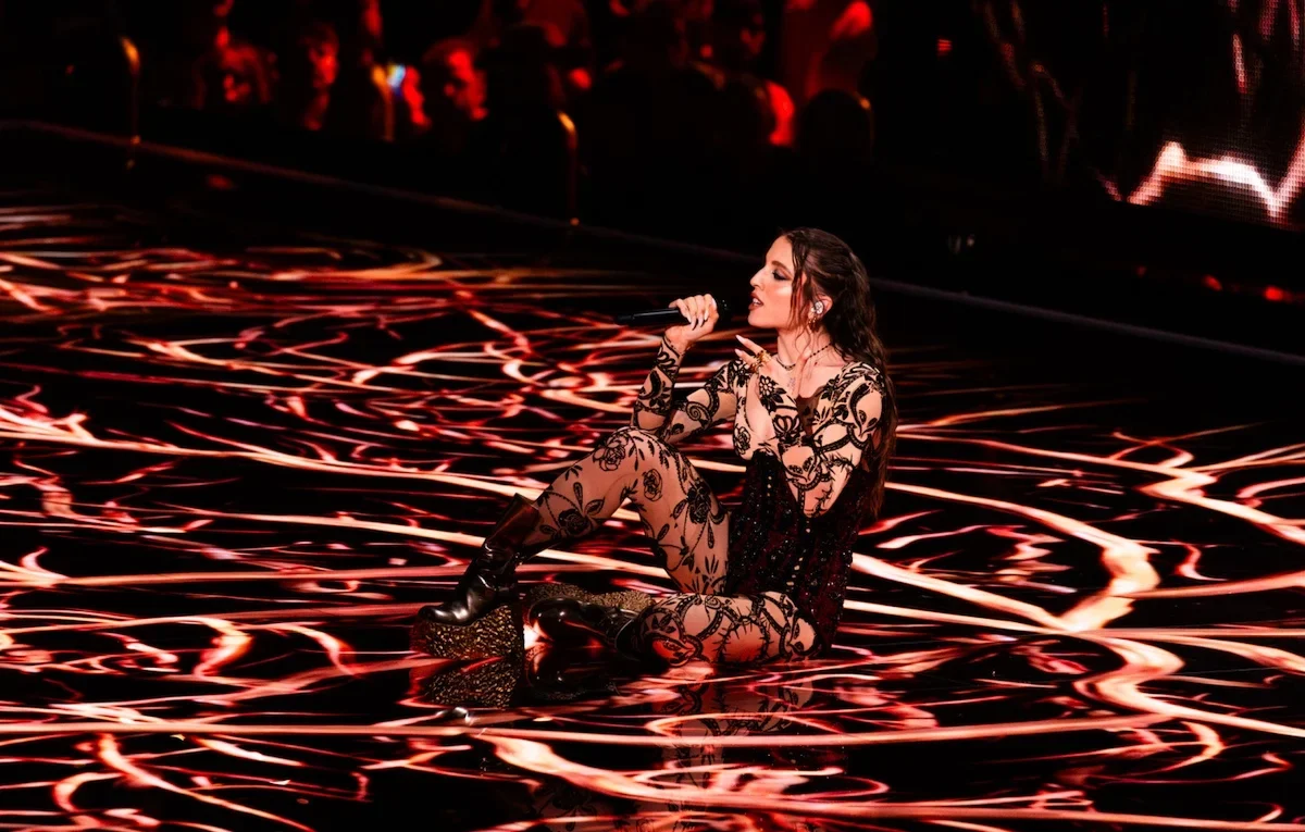 Angelina Mango sitting on a glossy floor swirling with red and white light, singing into the microphone – Angelina Mango at Eurovision 2024, Malmö, Sweden – concert stage design