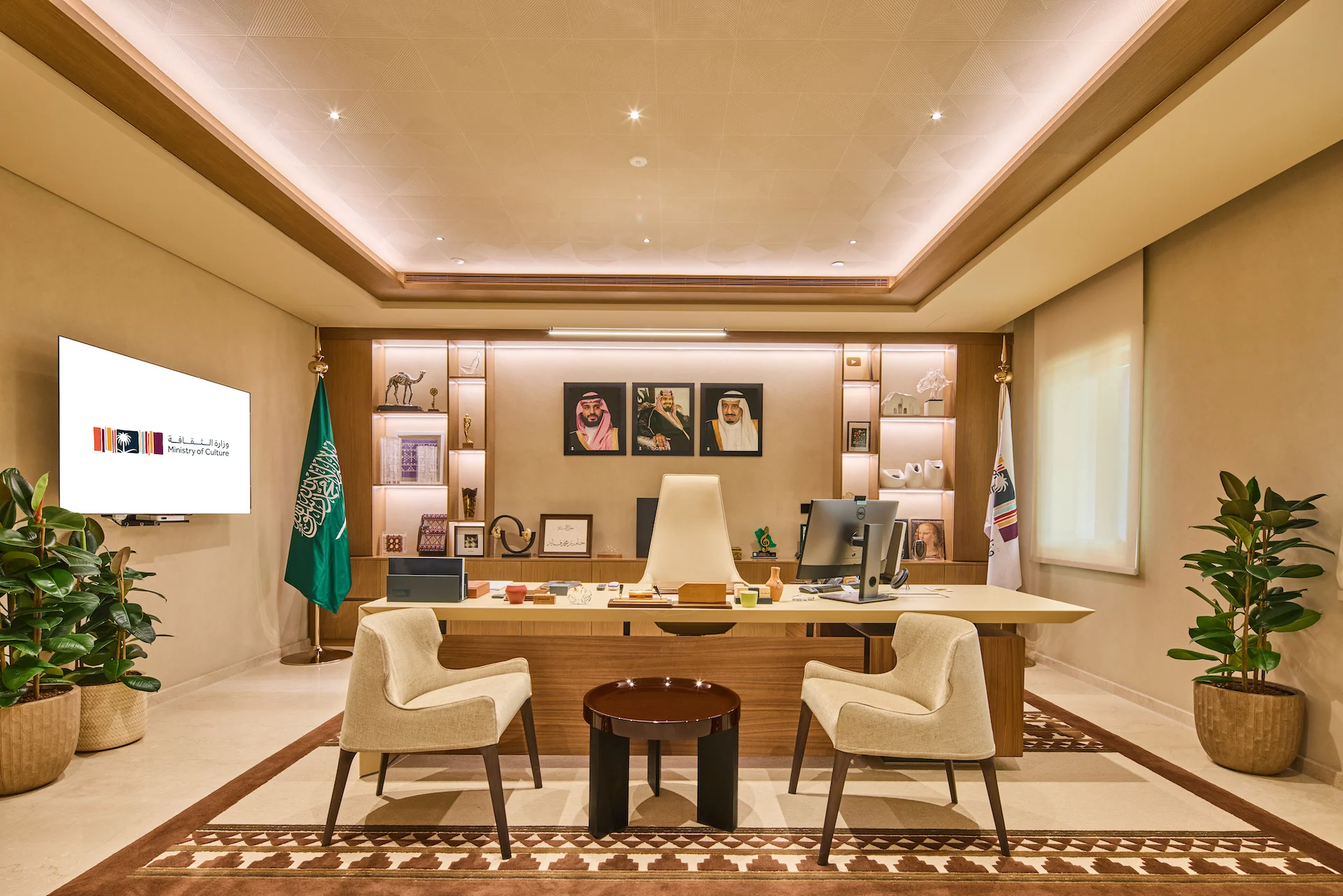 Executive office with a wooden desk, backlit shelving, framed portraits, flags and a patterned rug – MOC Headquarters, Diriyah, Saudi Arabia, 2026 – interior design
