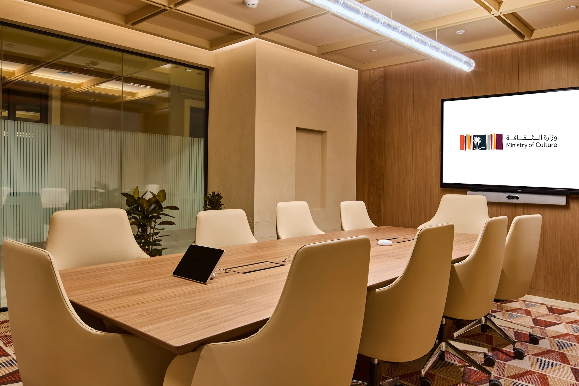 Meeting room with a long wooden table, cream chairs, wood-panelled wall and a screen showing the Ministry logo – MOC Headquarters, Diriyah, Saudi Arabia, 2026 – interior design