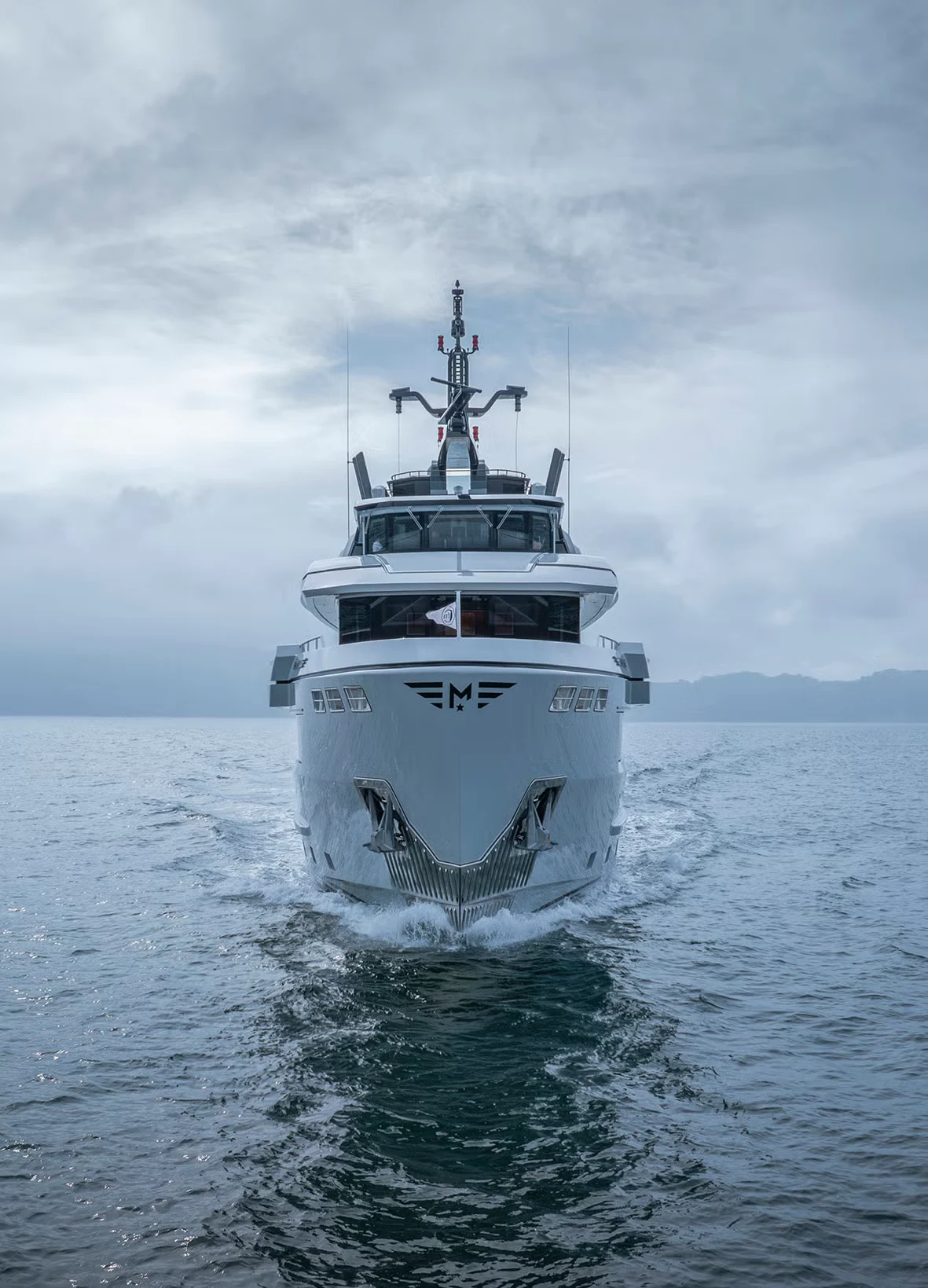 Vista frontale di un superyacht grigio che naviga verso l'obiettivo su acque calme sotto un cielo nuvoloso