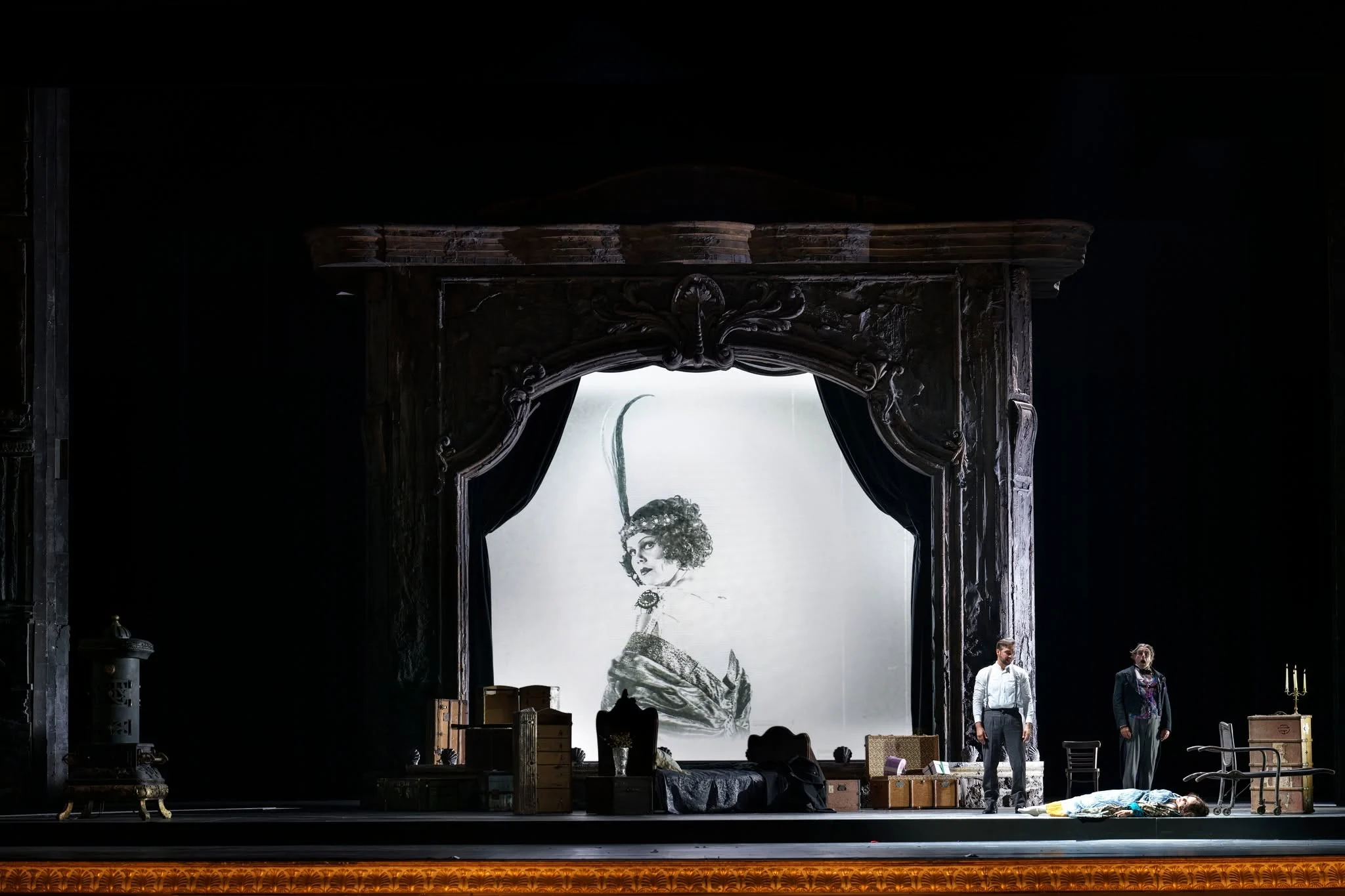 Carved stage portal framing a large sketched portrait of a diva, trunks and performers in front – Adriana Lecouvreur at Opéra de Monte-Carlo, Monte Carlo, Monaco, 2026 – set design