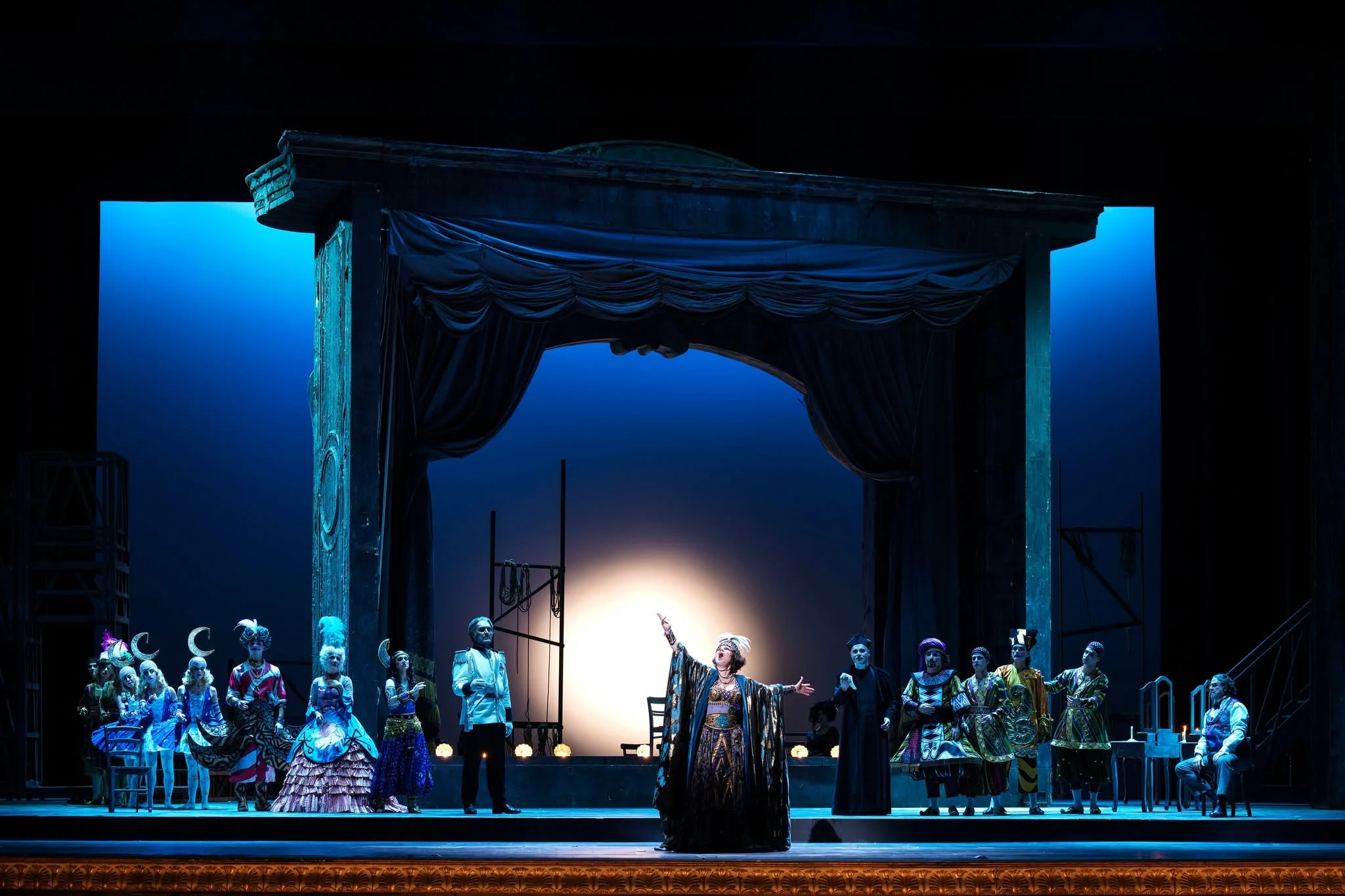 Adriana Lecouvreur at San Carlo: singer before a draped stage frame, costumed cast under deep blue light – Adriana Lecouvreur at Opéra de Monte-Carlo, Monte Carlo, Monaco, 2026 – set design