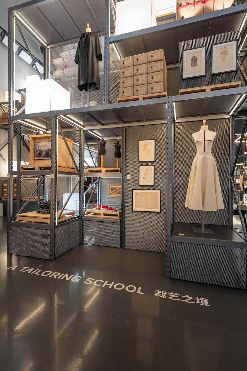 A Tailoring School section: white dress form, framed sketches and wooden crates on metal shelving – Max Mara The Max! at Long Museum, Shanghai, China, 2026 – exhibition design