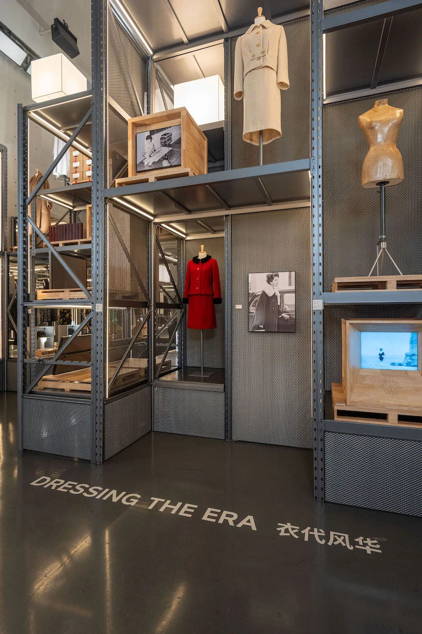 Dressing the Era section: red suit, beige suit and a tailor's dummy on metal shelving with wooden crates – Max Mara The Max! at Long Museum, Shanghai, China, 2026 – exhibition design