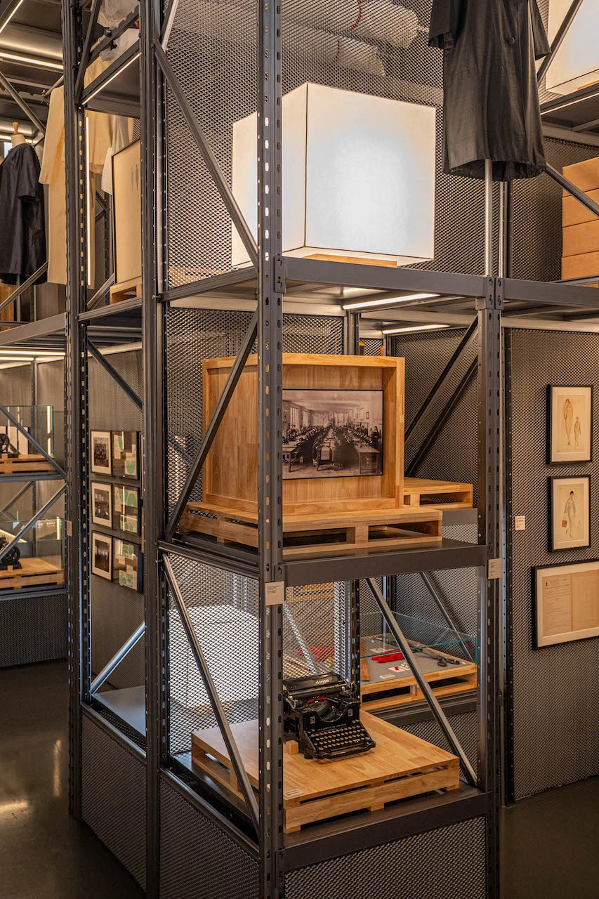 Tall metal shelving tower with a cube lamp, a framed archival photo and a vintage typewriter on wooden pallets – Max Mara The Max! at Long Museum, Shanghai, China, 2026 – exhibition design