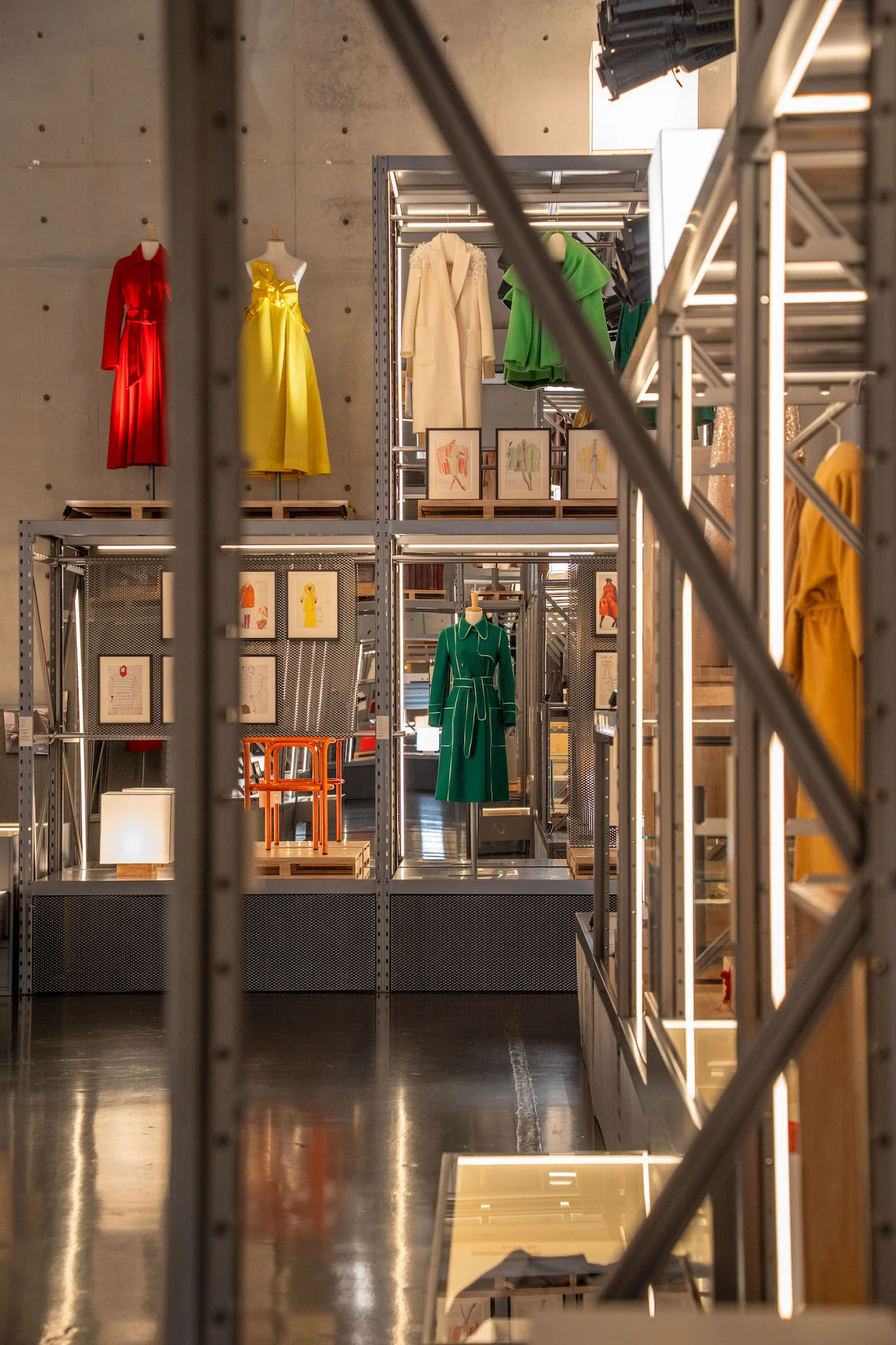 View through metal scaffolding to shelves of red, yellow and green garments against a concrete wall – Max Mara The Max! at Long Museum, Shanghai, China, 2026 – exhibition design