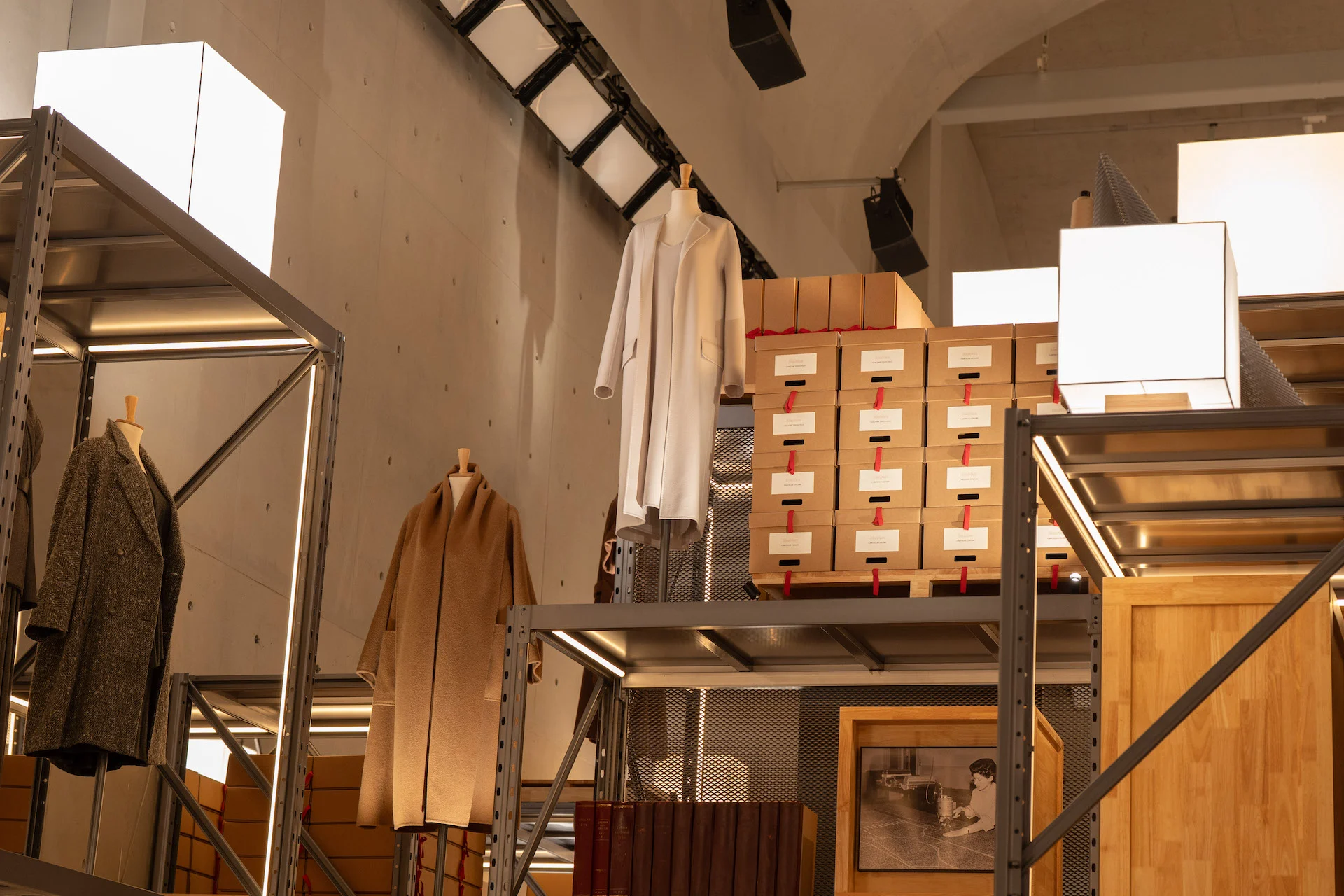 Upper levels of the shelving installation with coats, stacked archive boxes and cube lamps under a concrete vault – Max Mara The Max! at Long Museum, Shanghai, China, 2026 – exhibition design
