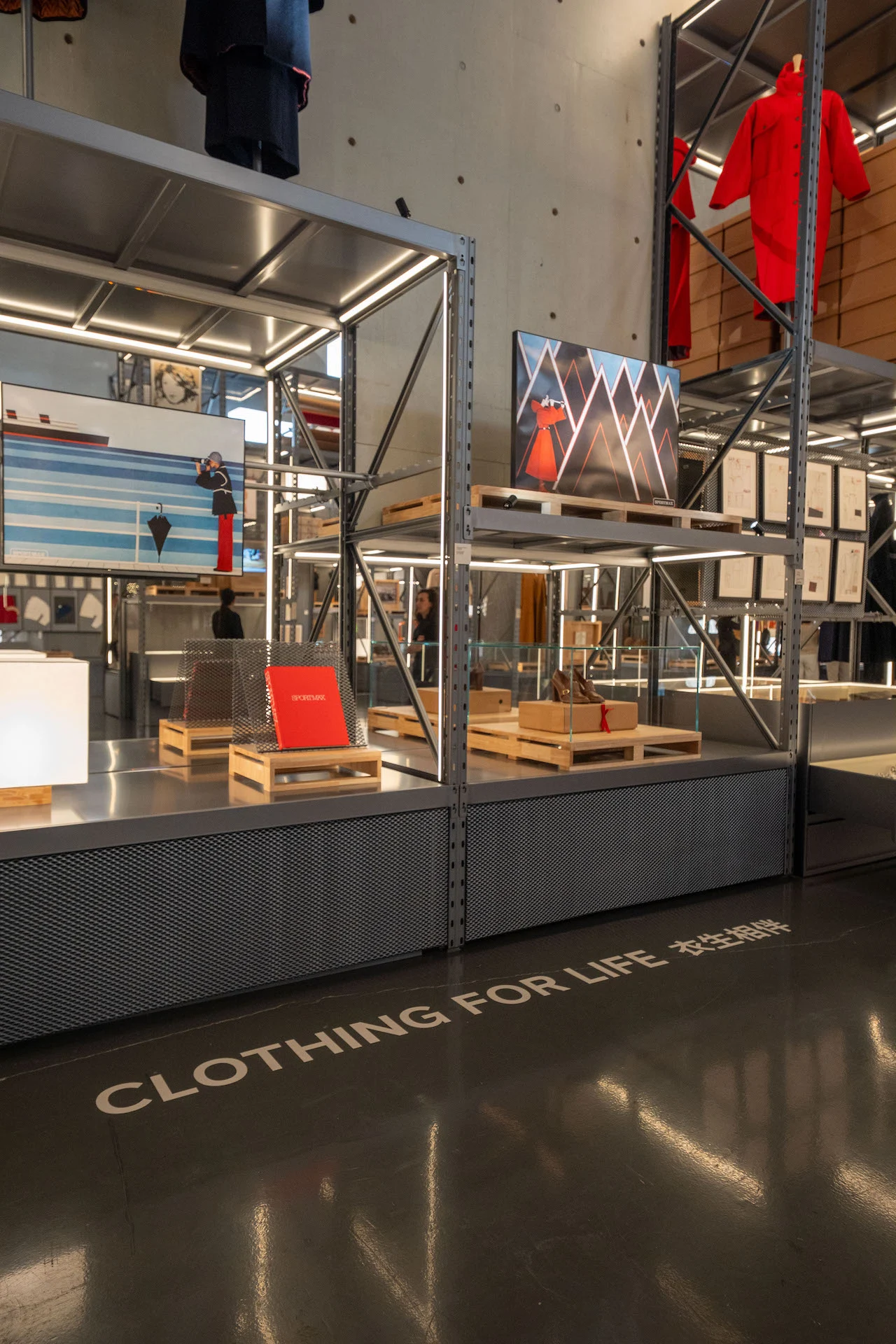 Clothing for Life section: metal shelves with red garments, artworks and books on wooden pallets – Max Mara The Max! at Long Museum, Shanghai, China, 2026 – exhibition design