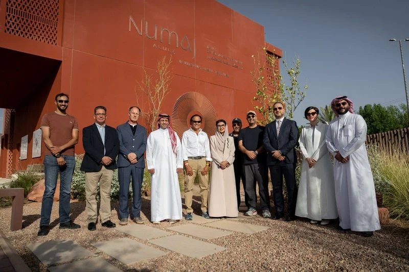 Group of people standing in front of the terracotta-red NUMAJ sign wall in a desert garden