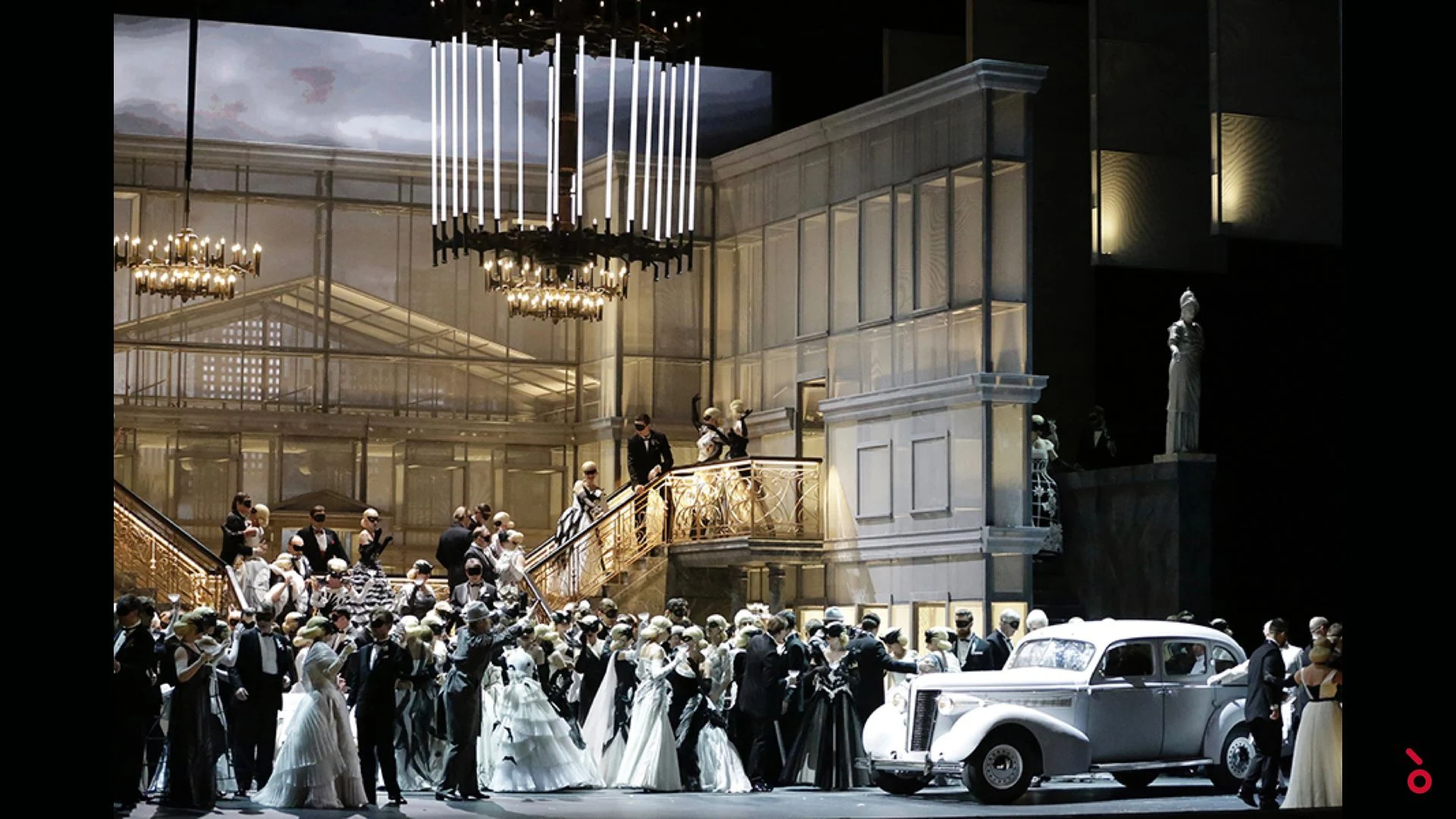 Ballroom scene with a grand staircase, crystal chandeliers, guests in evening dress and a vintage white car – Un Ballo in Maschera at the Bolshoi Theatre, Moscow, Russia, 2018 – opera set design