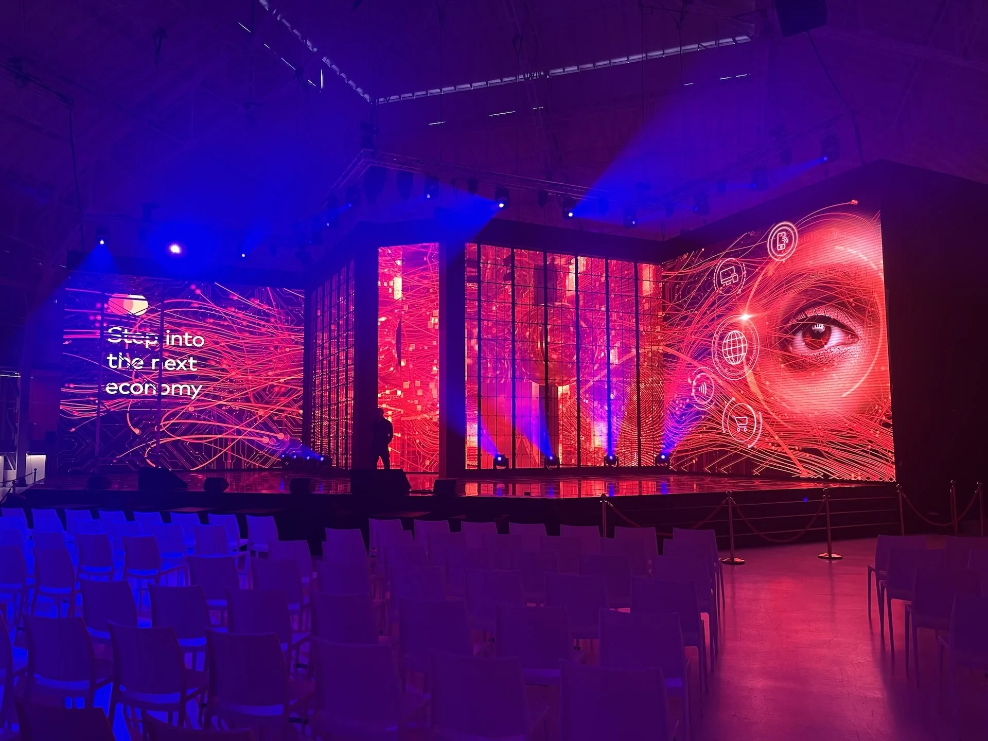 Stage with LED walls reading Step into the next economy, a giant eye graphic and rows of white chairs – Mastercard Innovation Forum 2023, Milan, Italy – event design